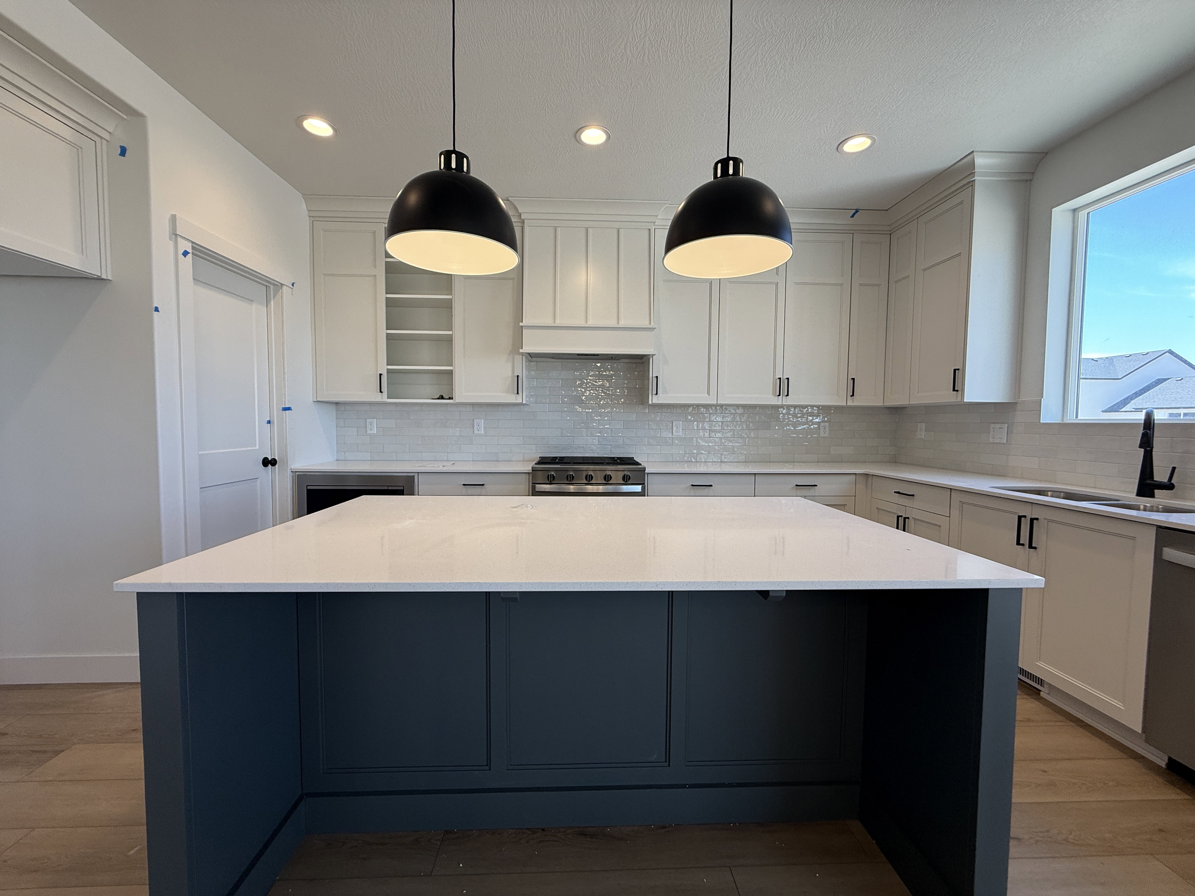 Kitchen featuring a spacious island with a white countertop and blue-painted base, two pendant light fixtures, white shaker-style cabinetry, and a subway tile backsplash