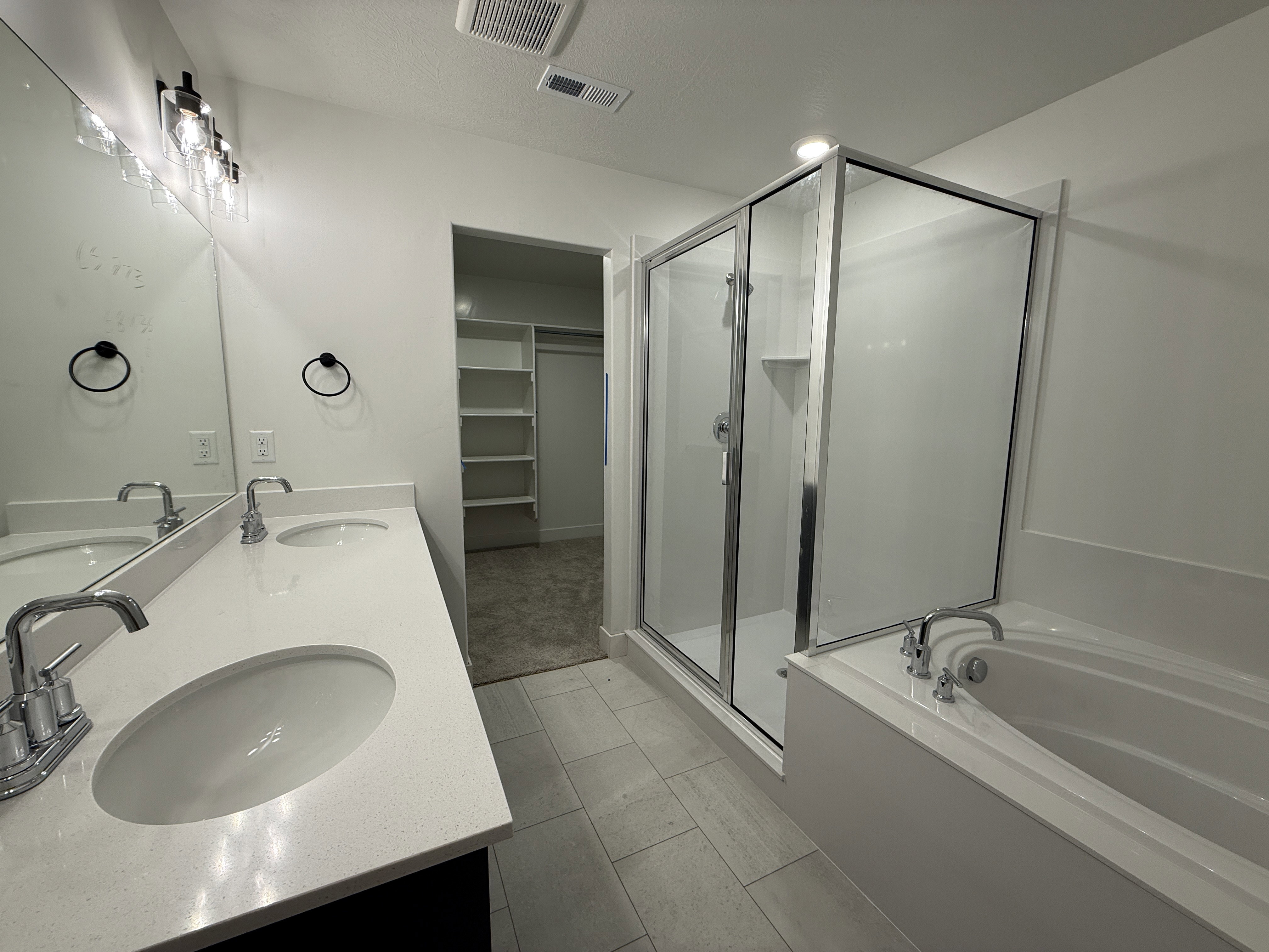 Bathroom featuring a dual vanity with undermount sinks, quartz countertops, a glass-enclosed shower, a built-in soaking tub, and tile flooring
