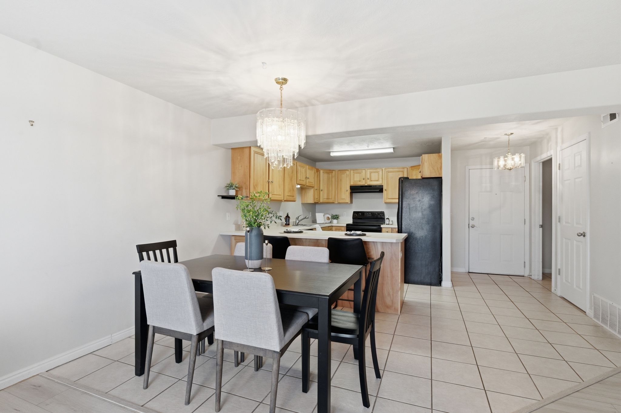 Dining area with a crystal chandelier, open concept kitchen access, light wood cabinetry, white countertops, and tile flooring