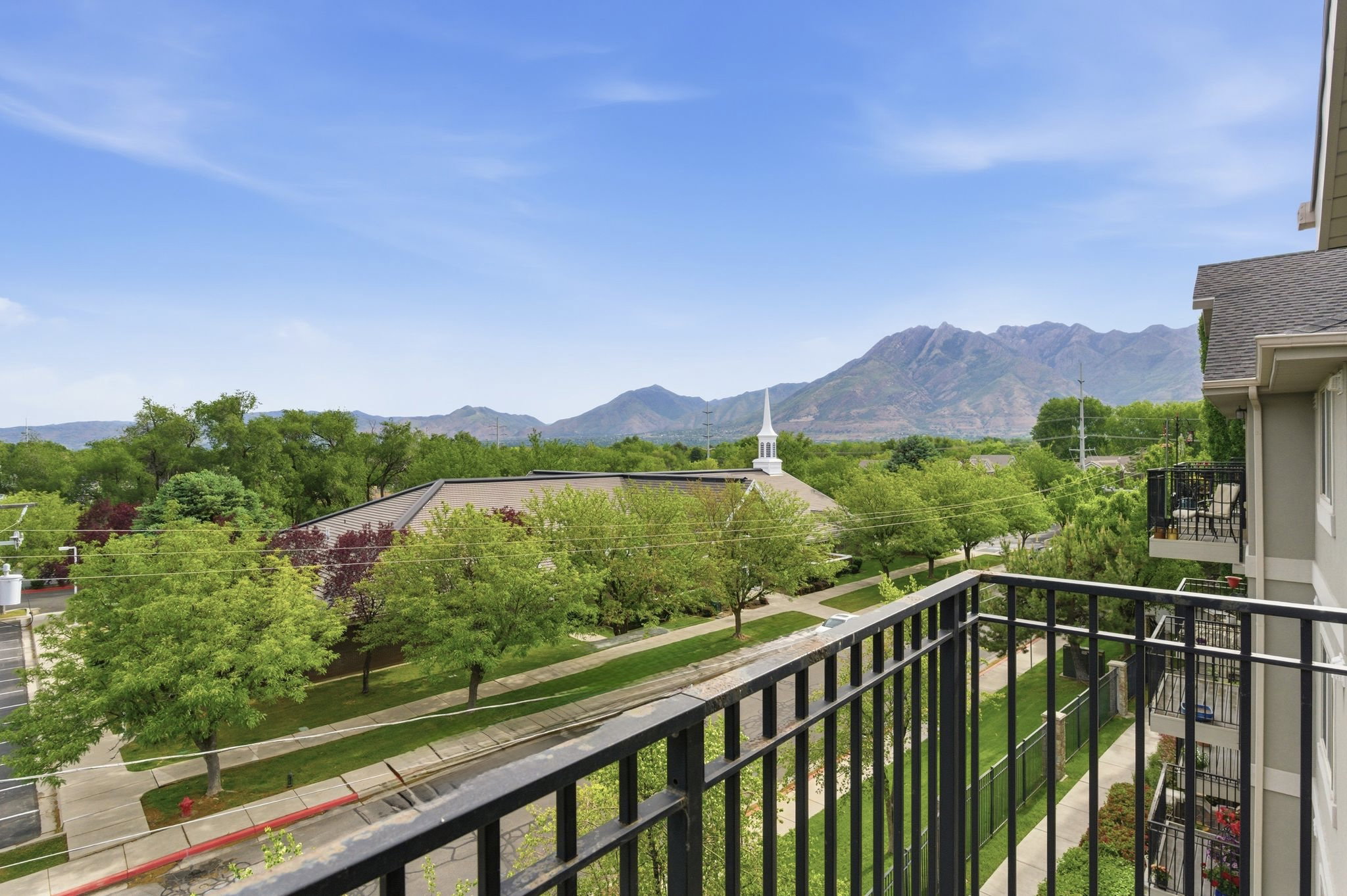 Balcony with black metal railings overlooking a tree-lined street and distant mountains