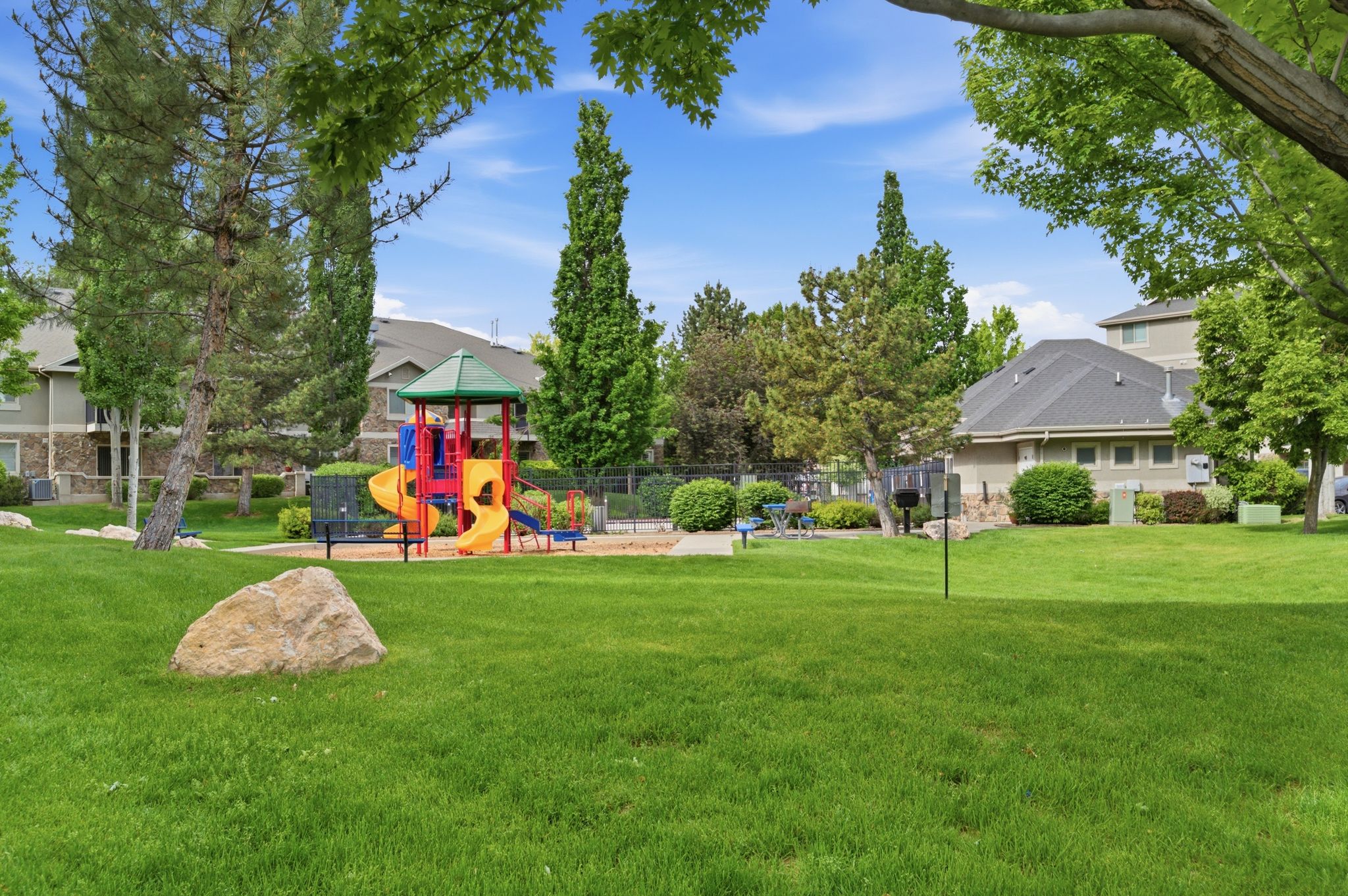 Community green space featuring a vibrant multi-colored playground, mature trees, and manicured lawn