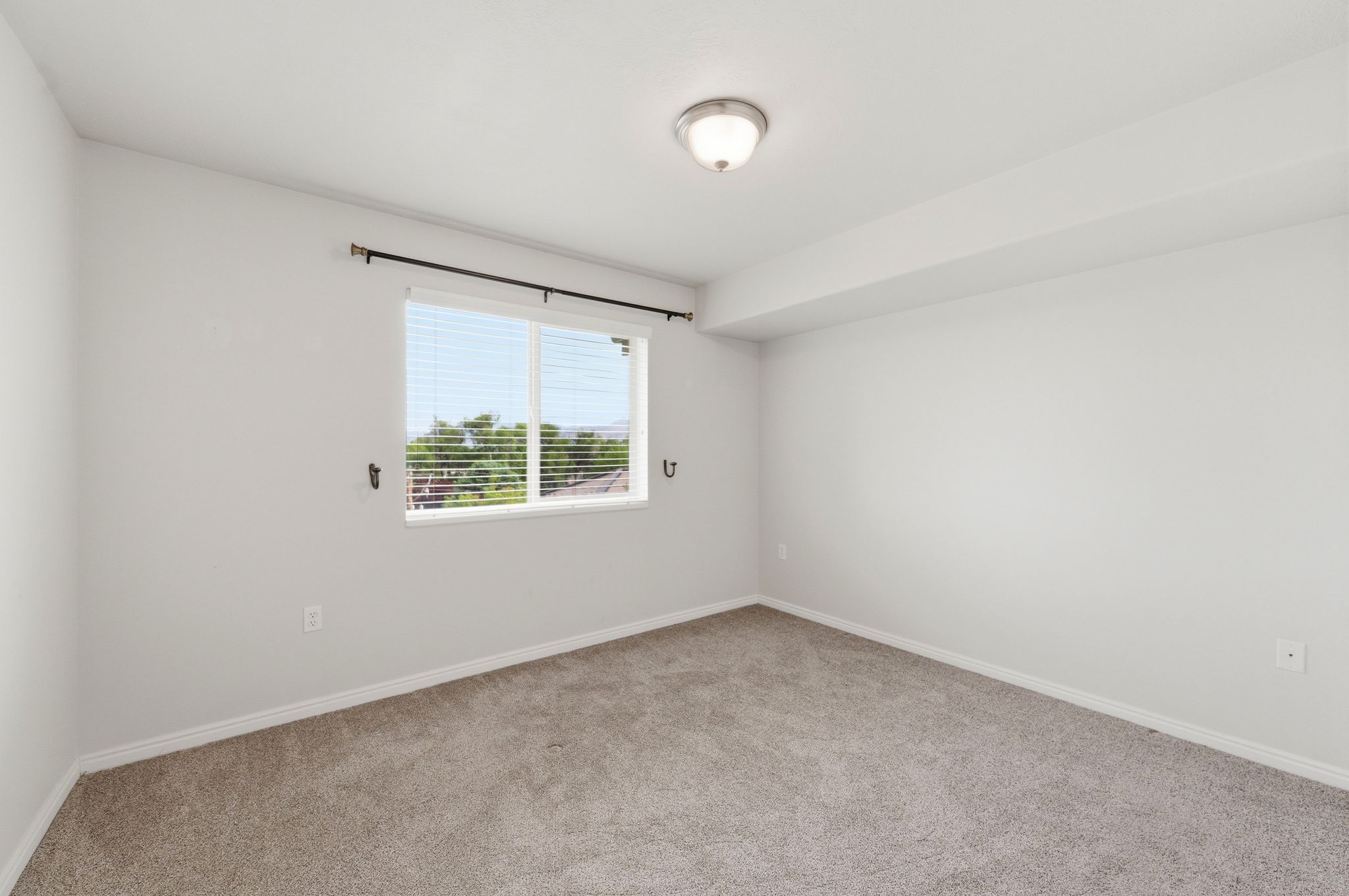 Guest bedroom featuring a window with blinds, a ceiling-mounted light fixture, and white baseboards
