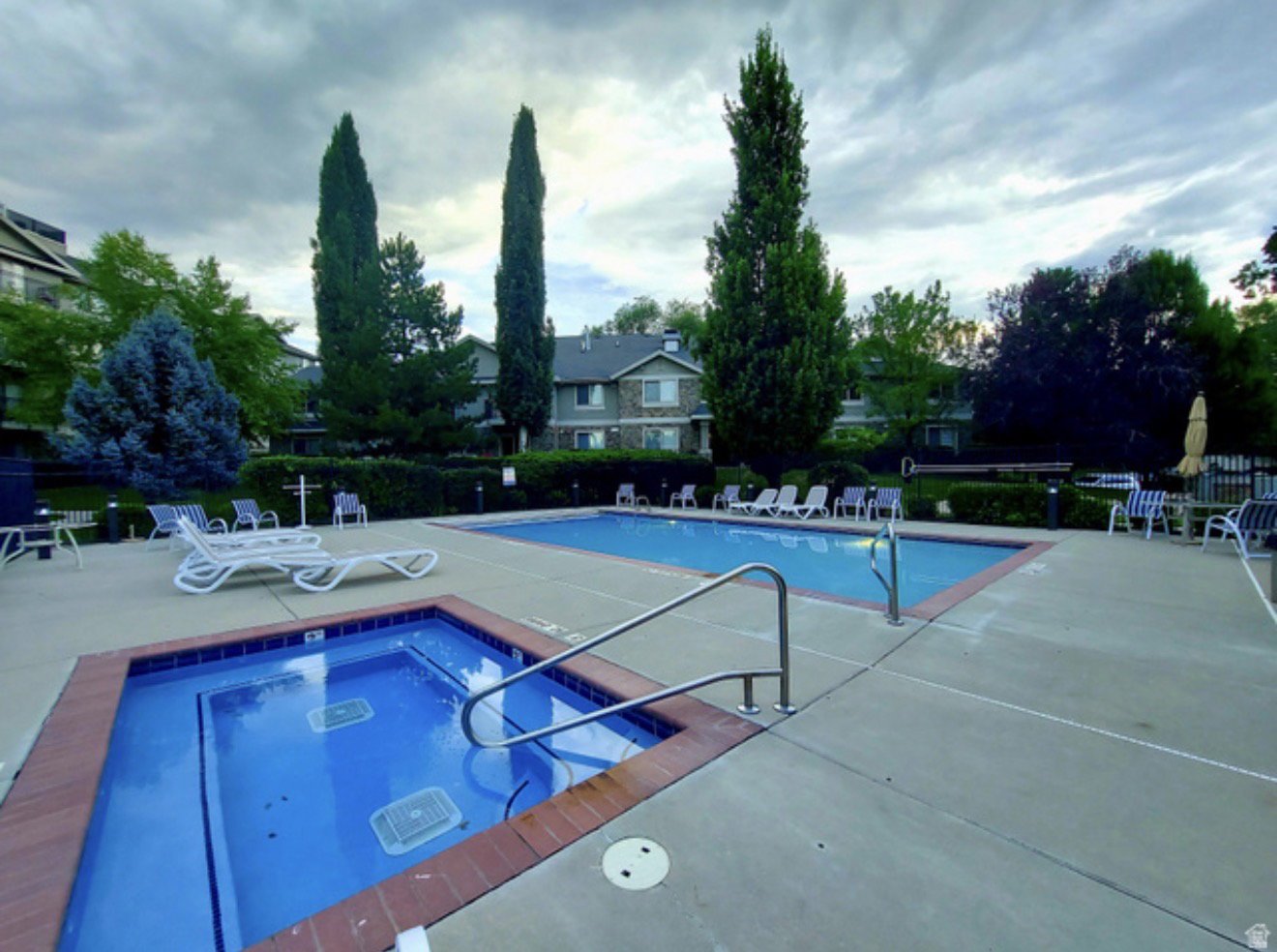 Resort-style pool and spa area featuring a concrete deck, an in-ground spa with brick coping, an in-ground swimming pool, and surrounding green landscaping