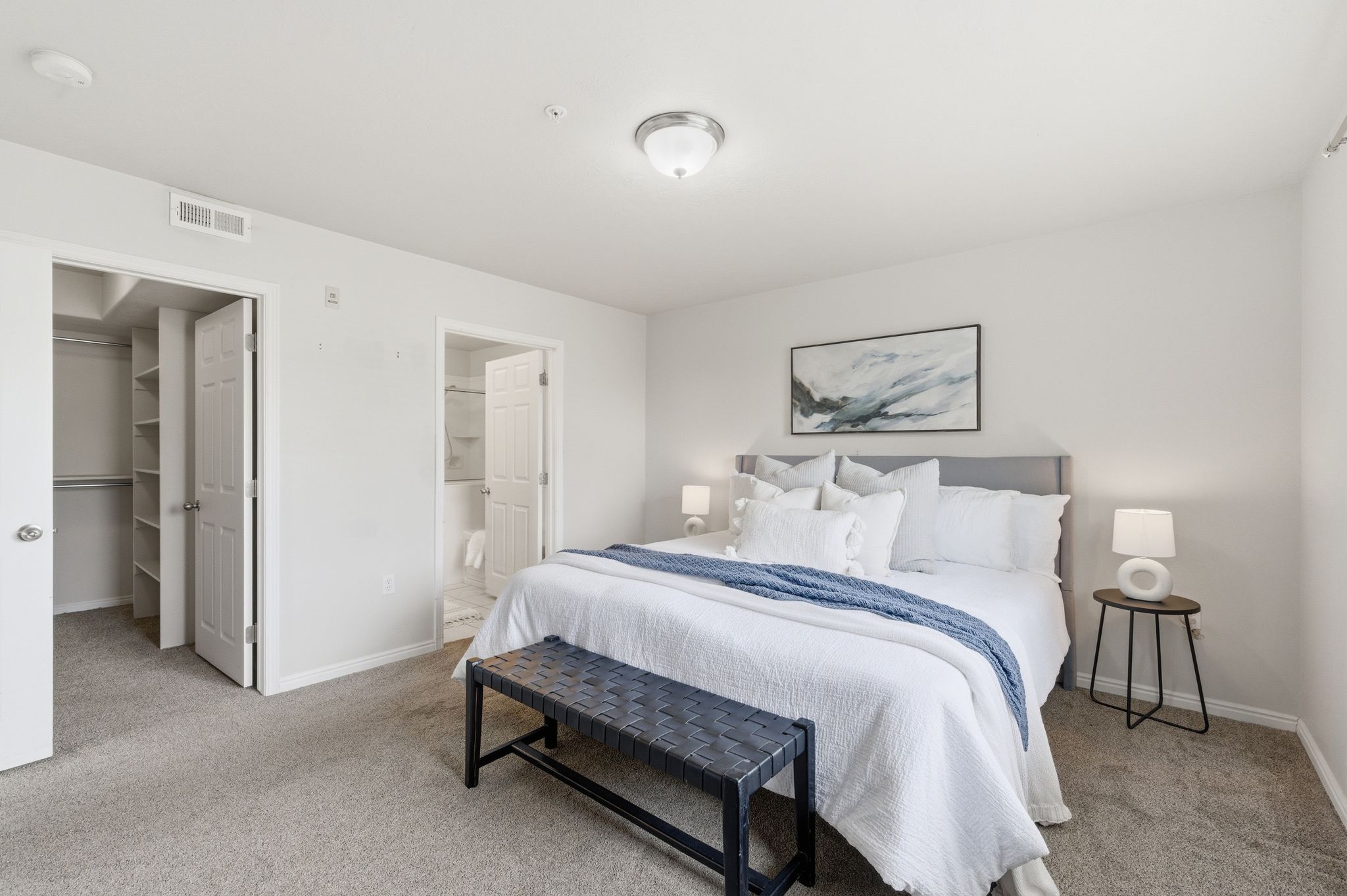 Primary bedroom featuring neutral wall tones, a built-in closet with shelving and hanging rods, and an en-suite bathroom entrance with a shower
