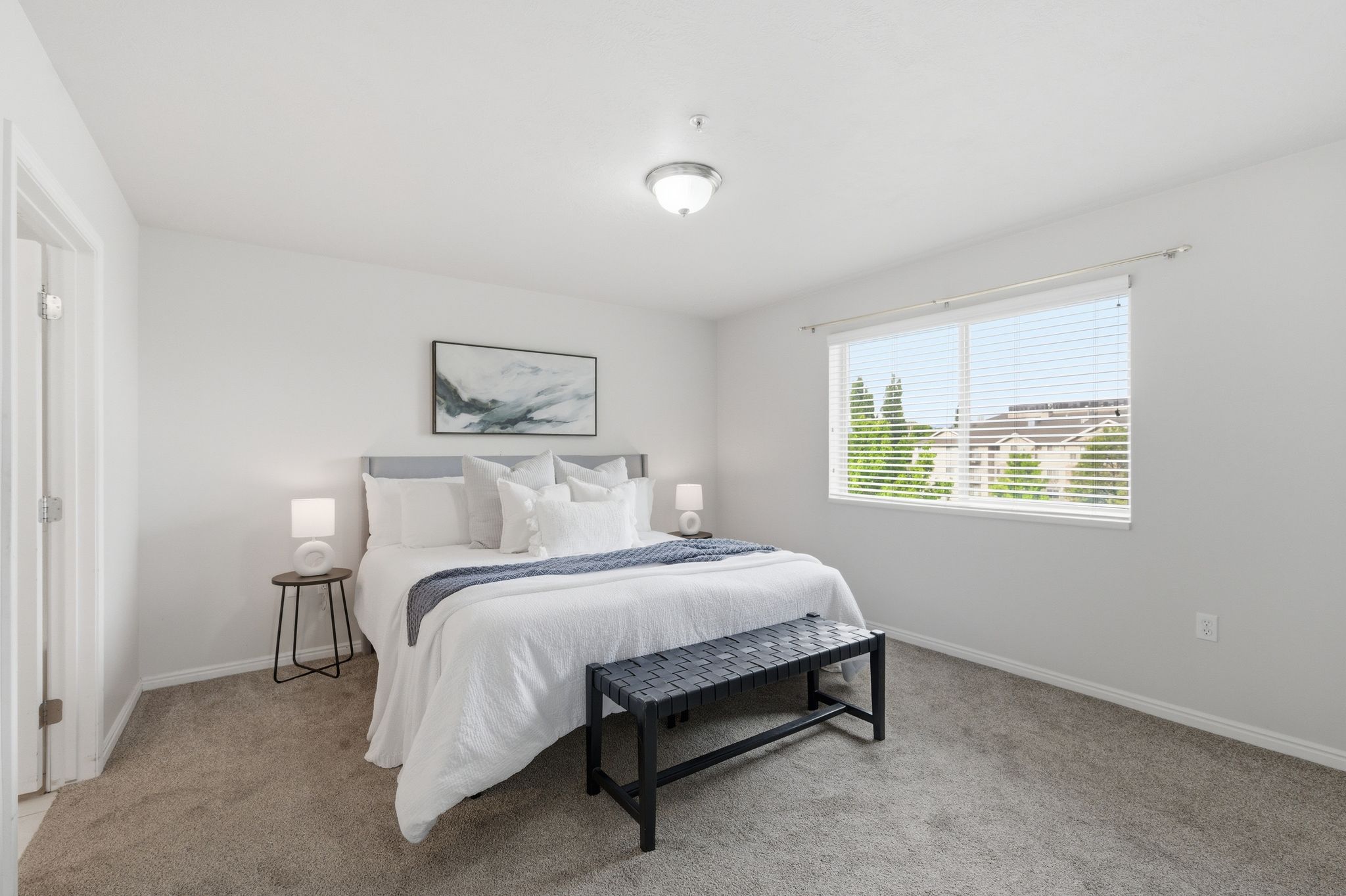 Primary bedroom featuring a broad window with white blinds, neutral wall paint, and gray carpet flooring