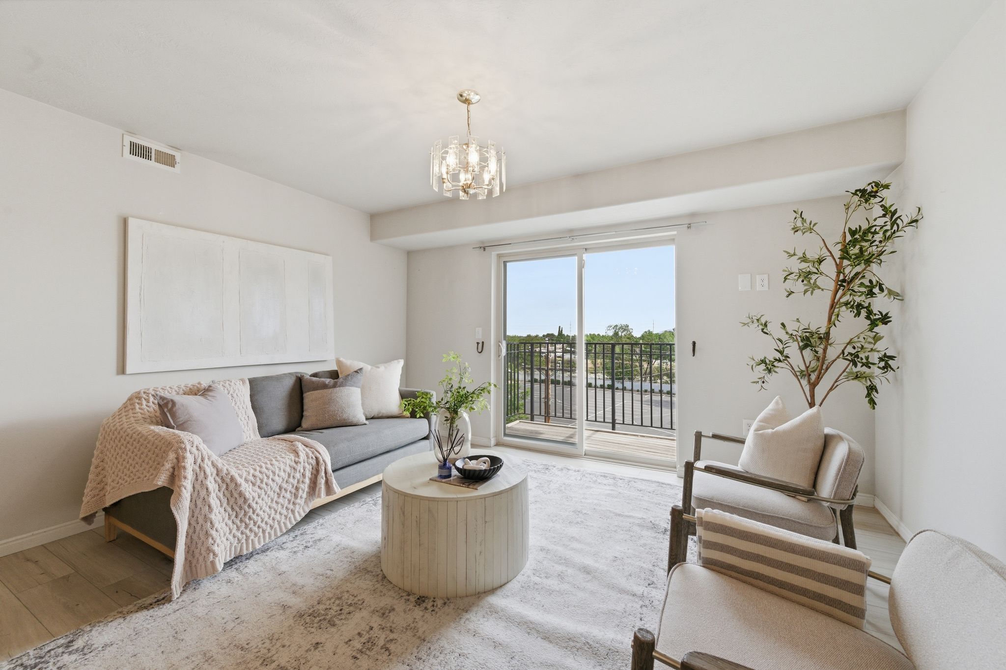 Bright living space featuring light wood-finish flooring, a contemporary chandelier, and direct access to an outdoor balcony through sliding glass door