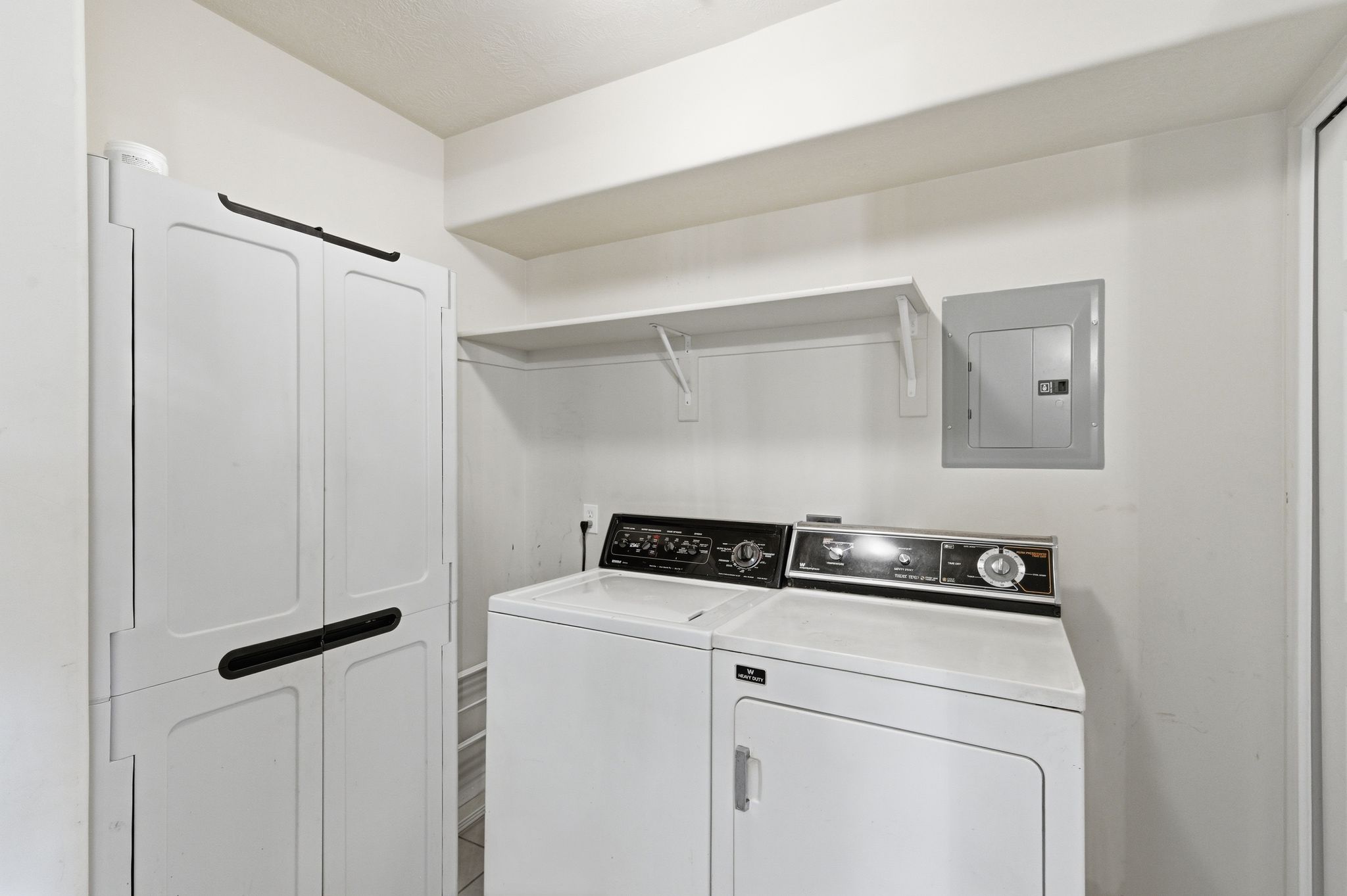 Dedicated laundry room with a white washing machine and dryer, a built-in wall shelf for storage, and a utility cabinet with dark handles