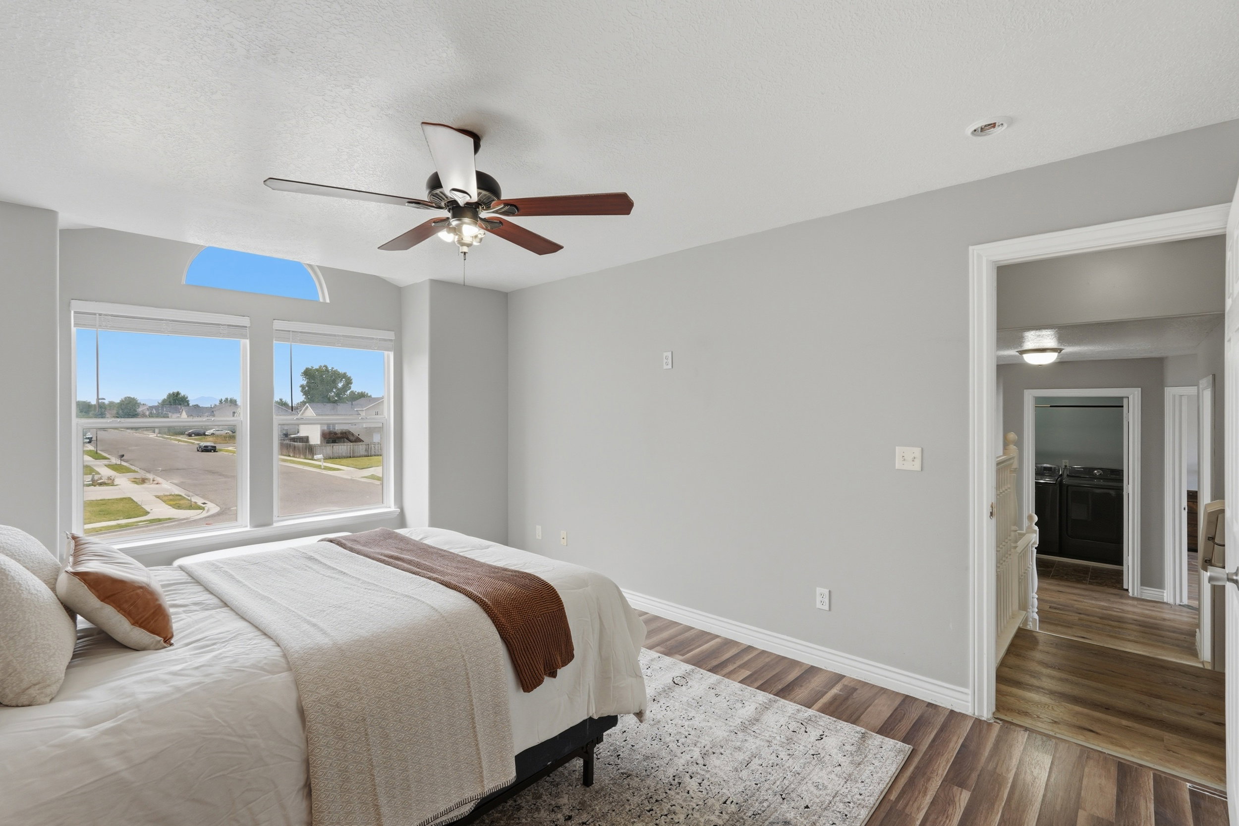 Spacious room featuring multiple large windows, an arched transom window, wood-finish flooring, and a ceiling fan with integrated lighting