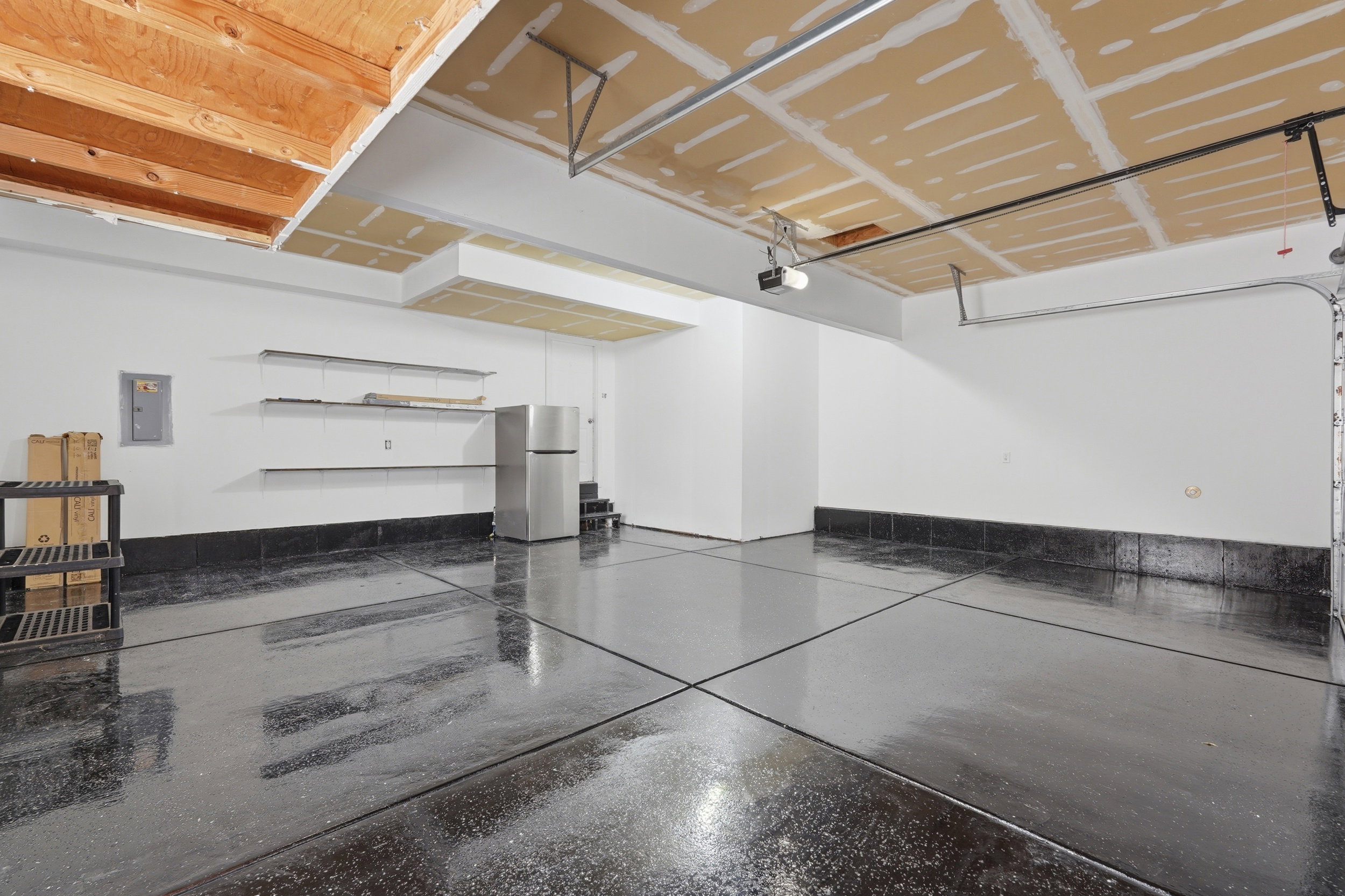 Spacious garage with high ceilings, exposed wood joists, and a durable dark epoxy floor finish