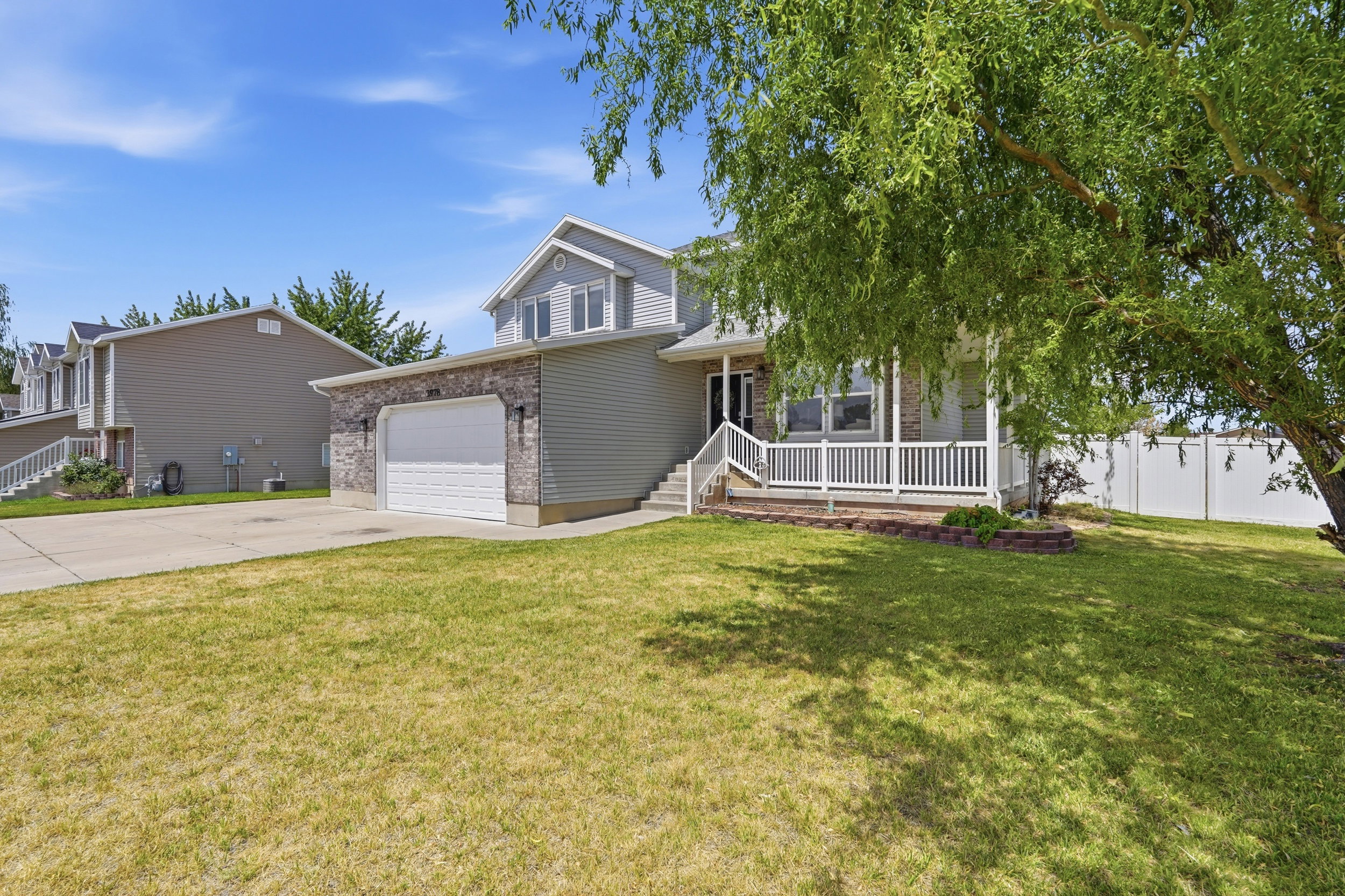 Two-story residence featuring a covered front porch with white railings, a two-car garage with stone veneer accents, and a concrete driveway