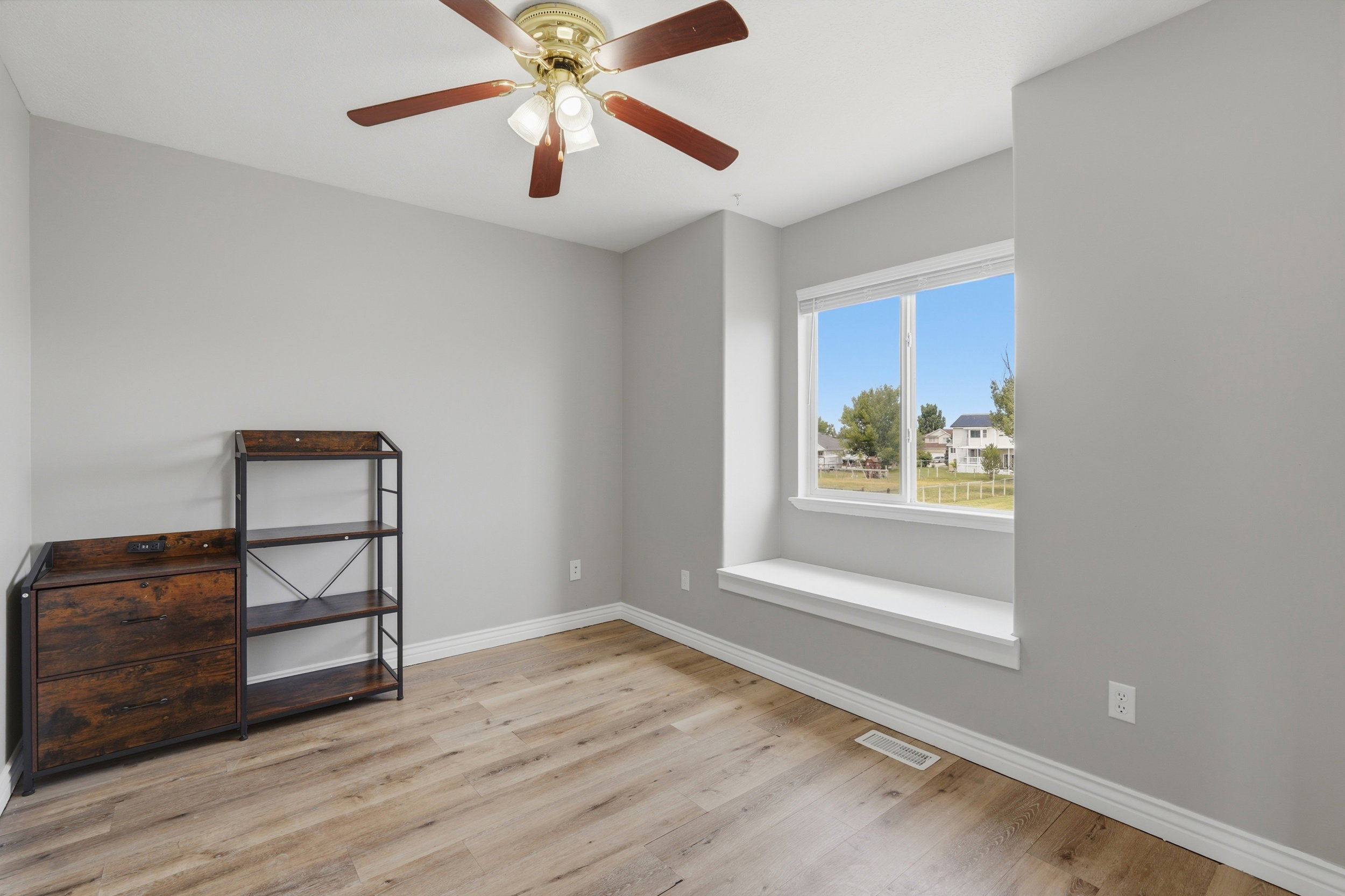 Bright room featuring wood-finish flooring, a ceiling fan with integrated lighting, and a window with a built-in sill