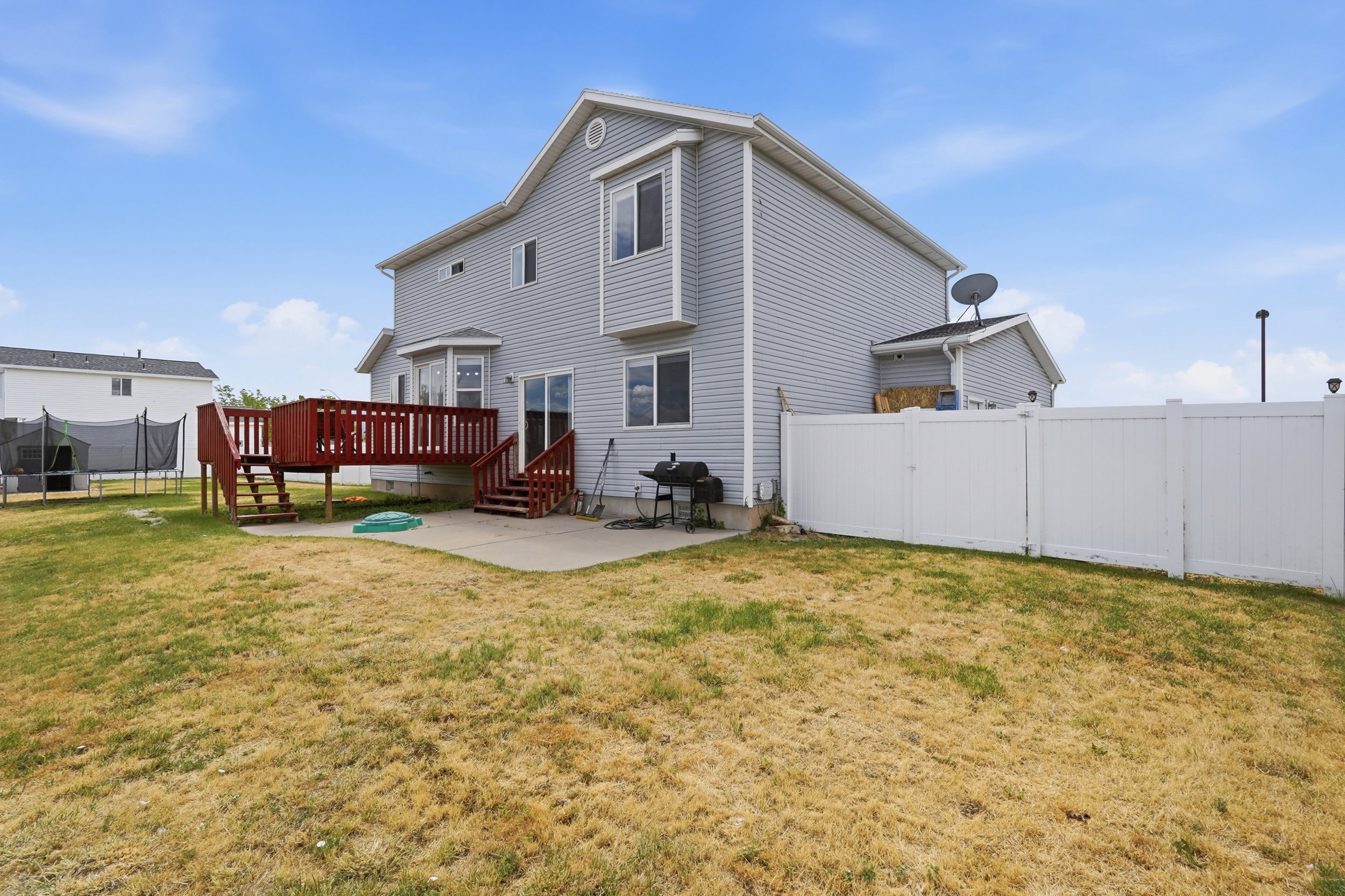 Rear exterior featuring a two-story design with light gray siding, a red-stained wood deck, and a ground-level concrete patio