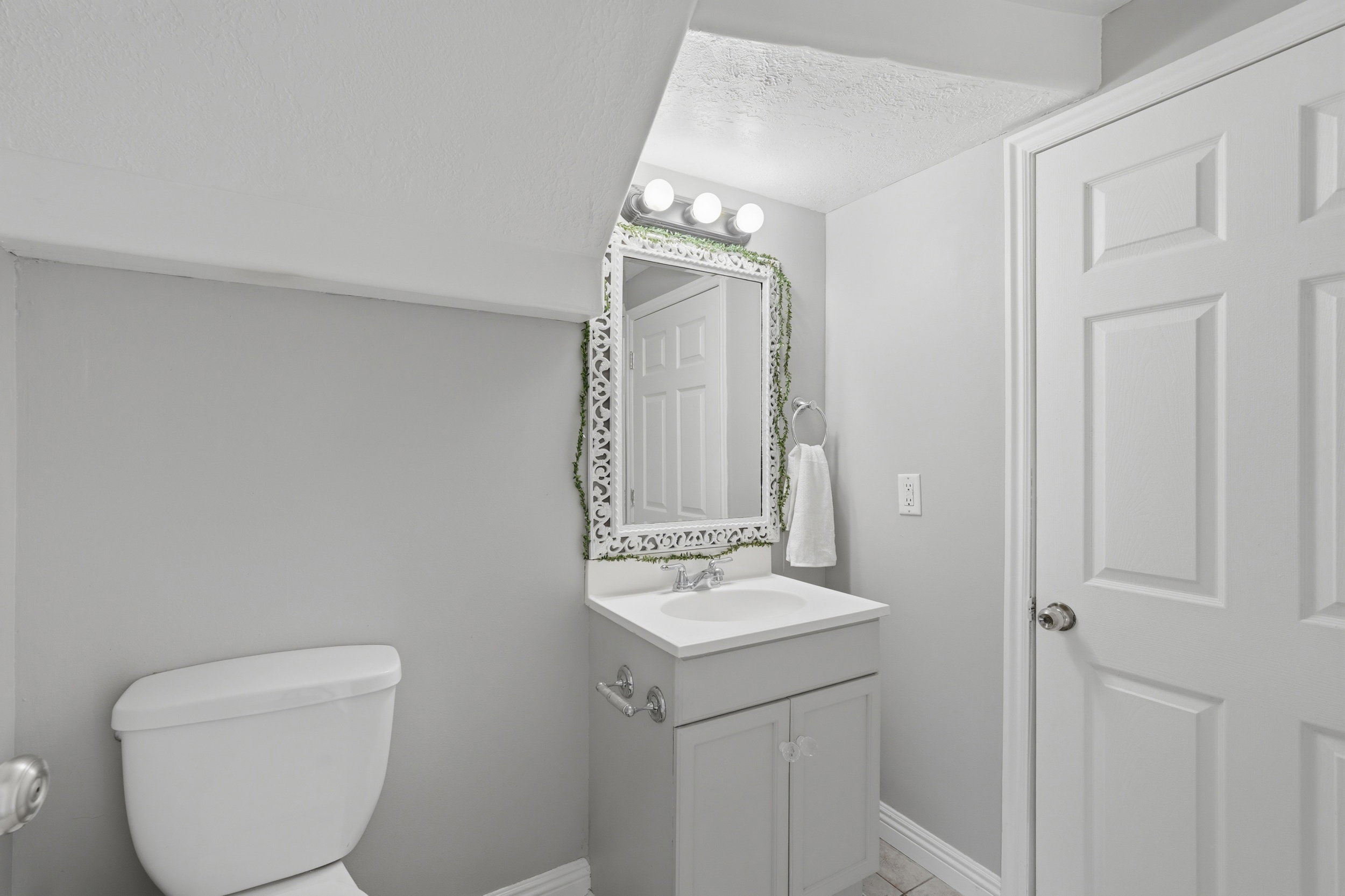 Bathroom vanity featuring a white sink, light gray cabinetry, and a decorative mirror with overhead lighting
