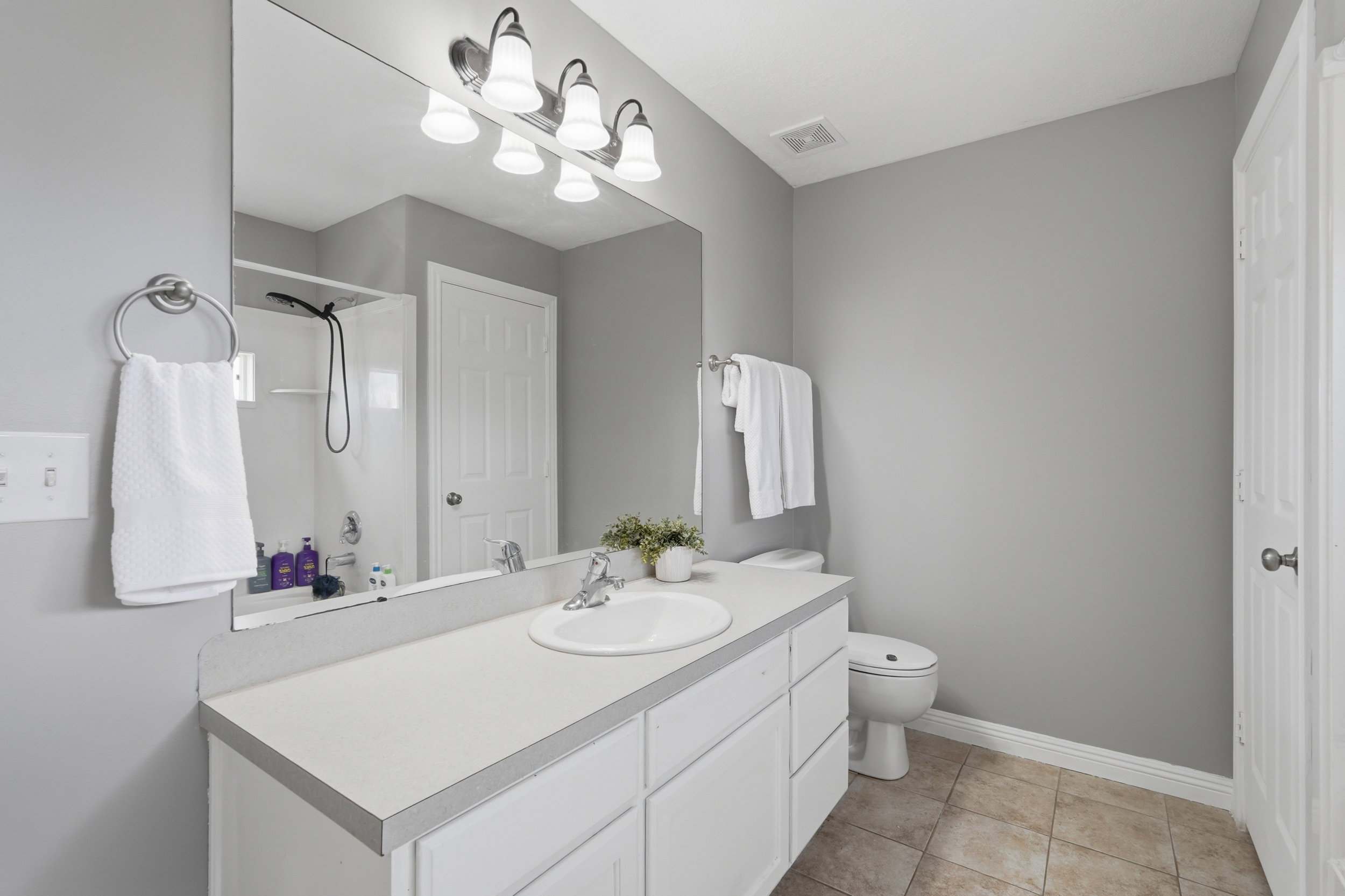 Full bathroom featuring a white vanity with an integrated sink, a large wall-mounted mirror, and a five-light vanity fixture