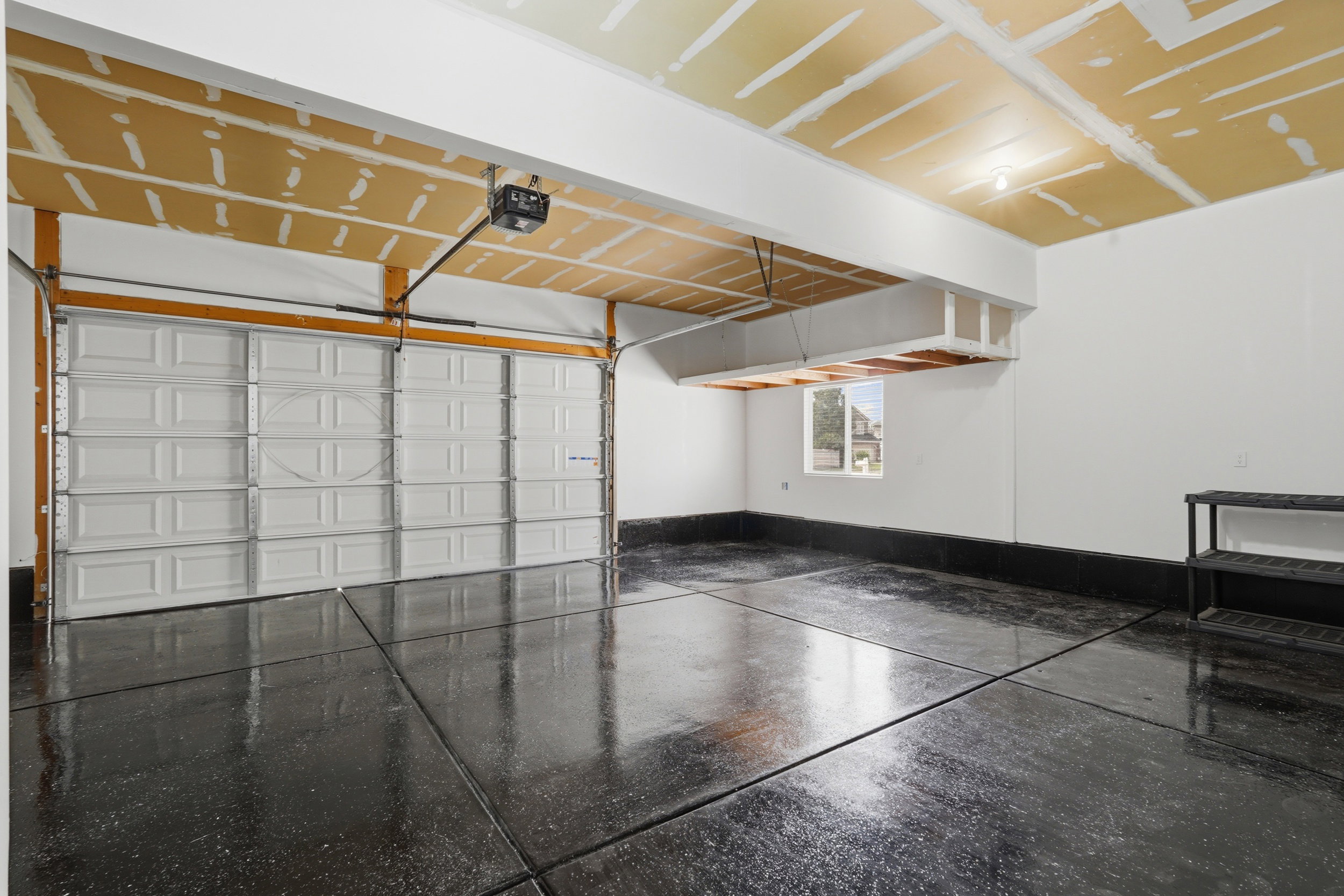 Spacious garage featuring a finished epoxy floor, white paneled garage door, and ample overhead storage