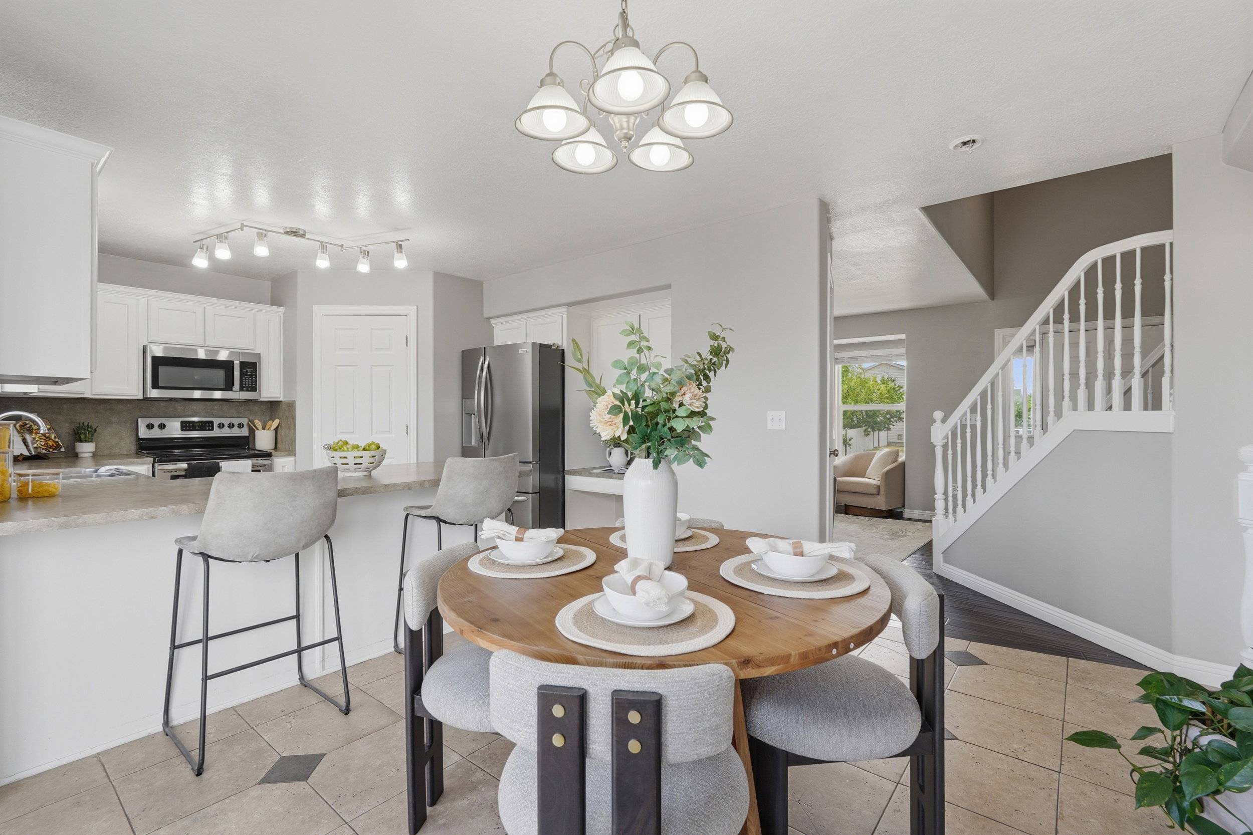 Open-concept dining area featuring a wood-finish round table, a five-light chandelier, and tile flooring with accent squares