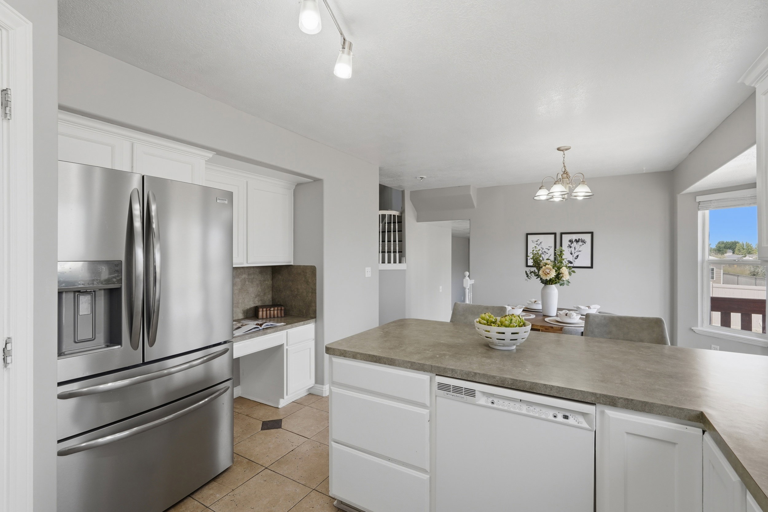 Open-concept kitchen with a stainless steel French door refrigerator, white cabinetry, and a stone-finish countertop island featuring an integrated dishwasher