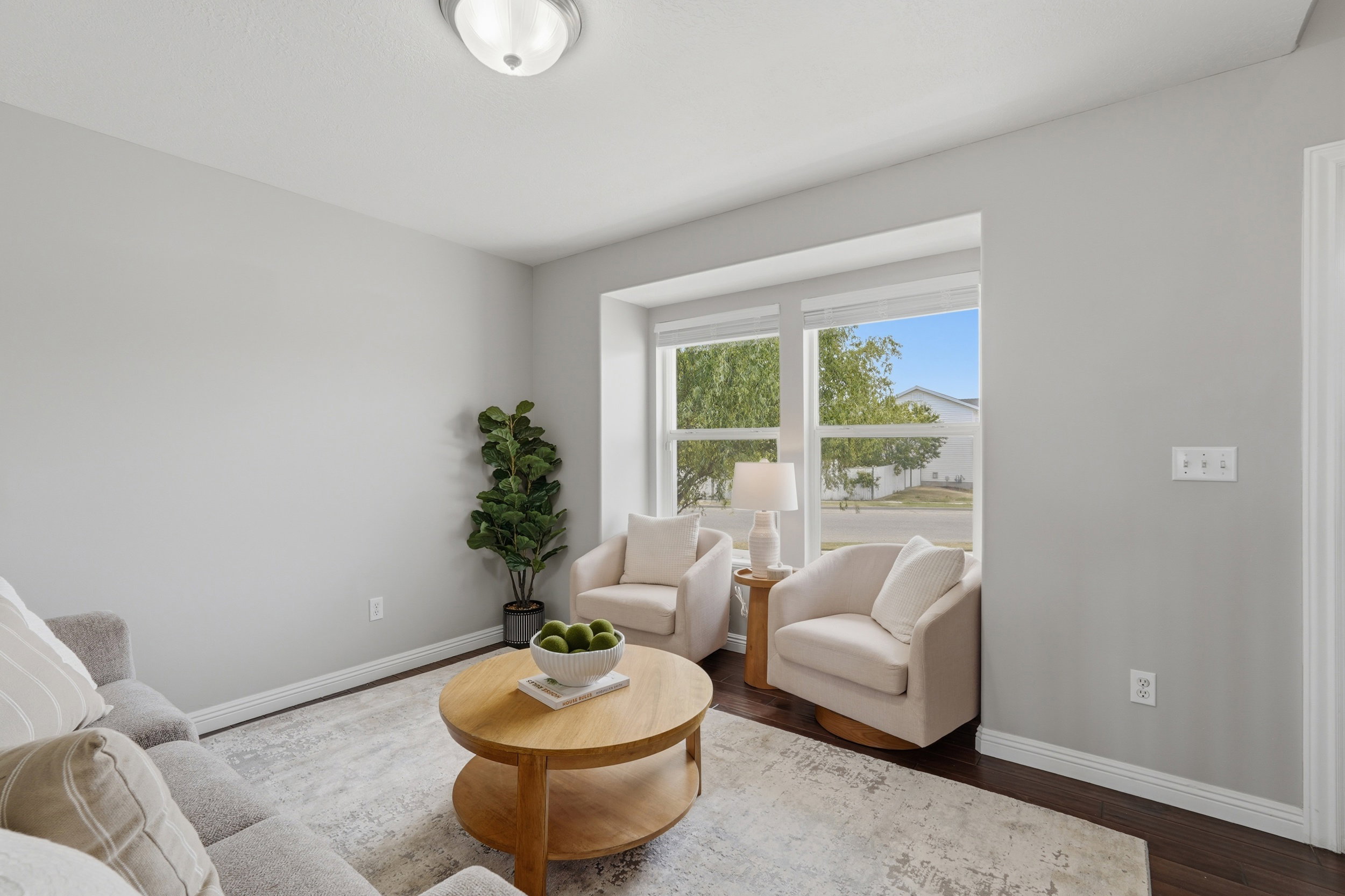 Living area featuring a bay window, dark wood-finish flooring, light grey wall color, white baseboards, and a flush-mount ceiling light