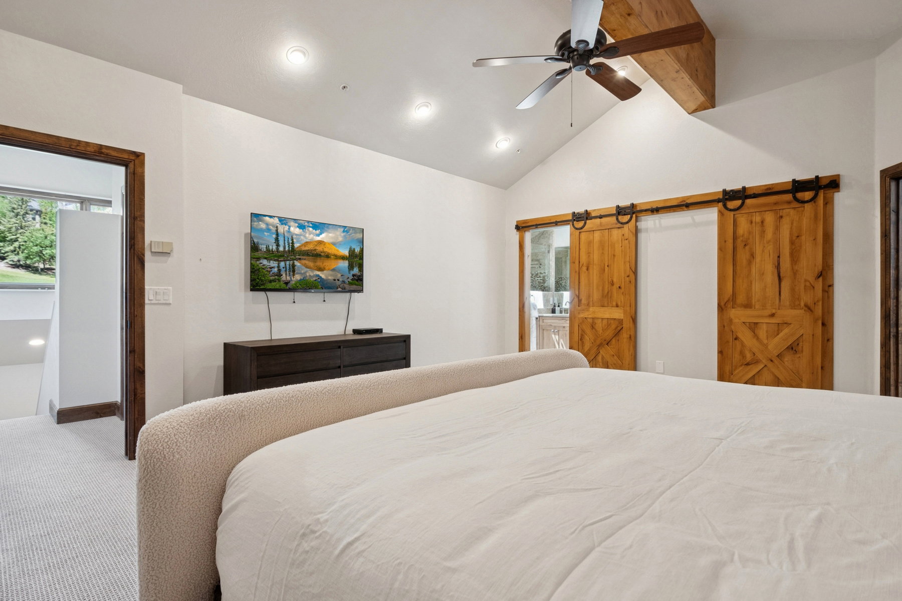 Vaulted ceiling with exposed wood beam and ceiling fan, recessed lighting, and barn doors with dark hardware