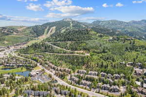 Expansive aerial showcasing a mountainous landscape with ski slopes, dense evergreen forests, and a community featuring residential properties, roads, and a pond