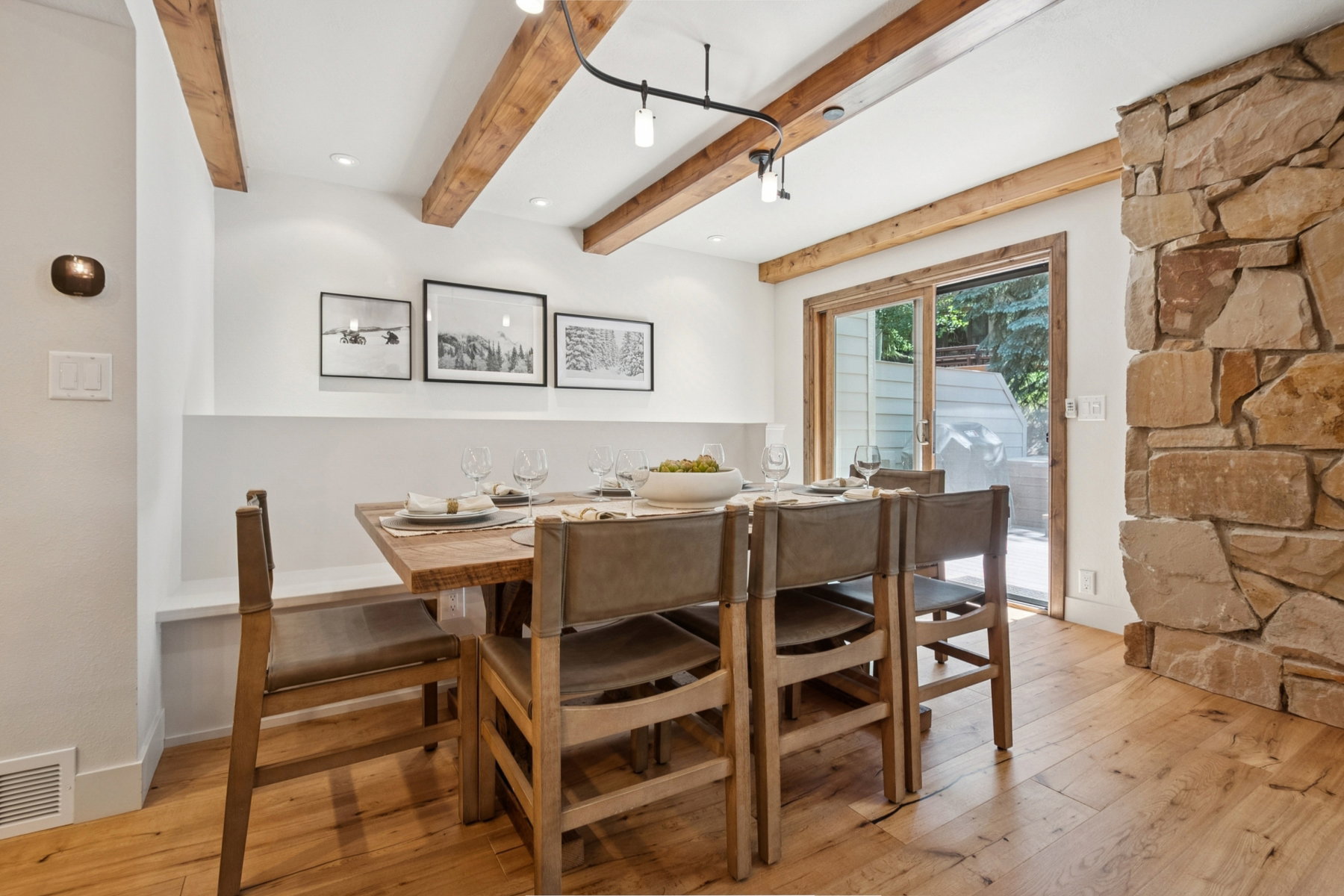 Dining area featuring exposed wood beams, a stone accent wall, wood-finish flooring, a built-in bench, and sliding glass door access to an outdoor area
