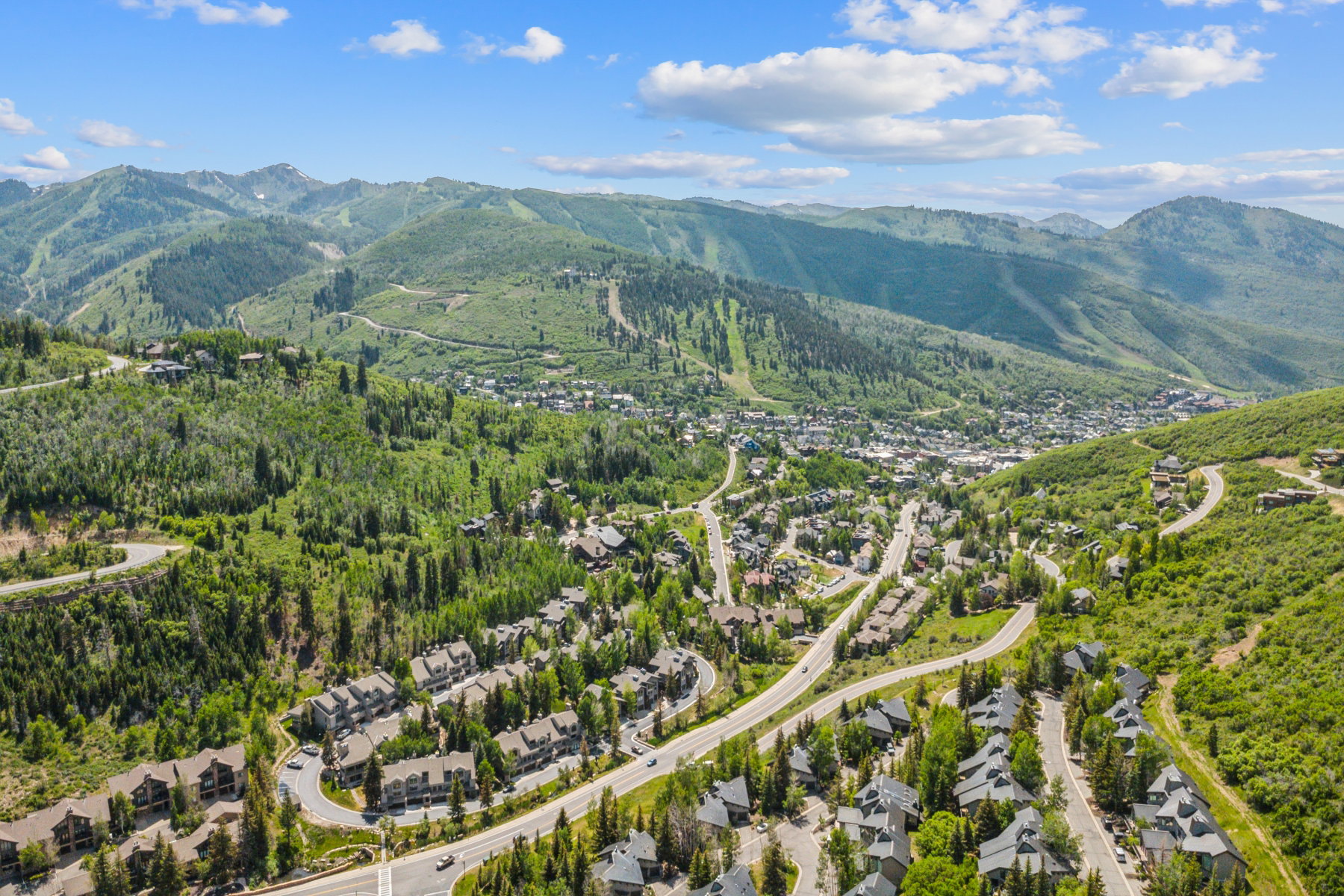 Expansive mountain landscape featuring a valley town, winding roads, and residential properties