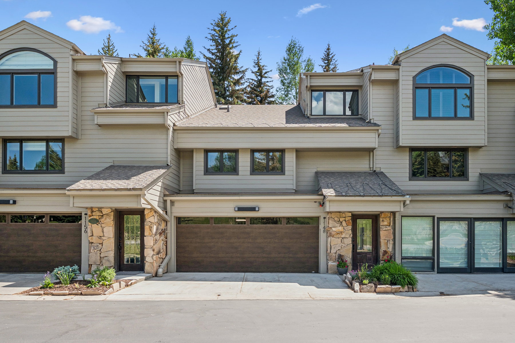 Multi-level townhome featuring stone accents, wood-finish garage doors, and dormer windows