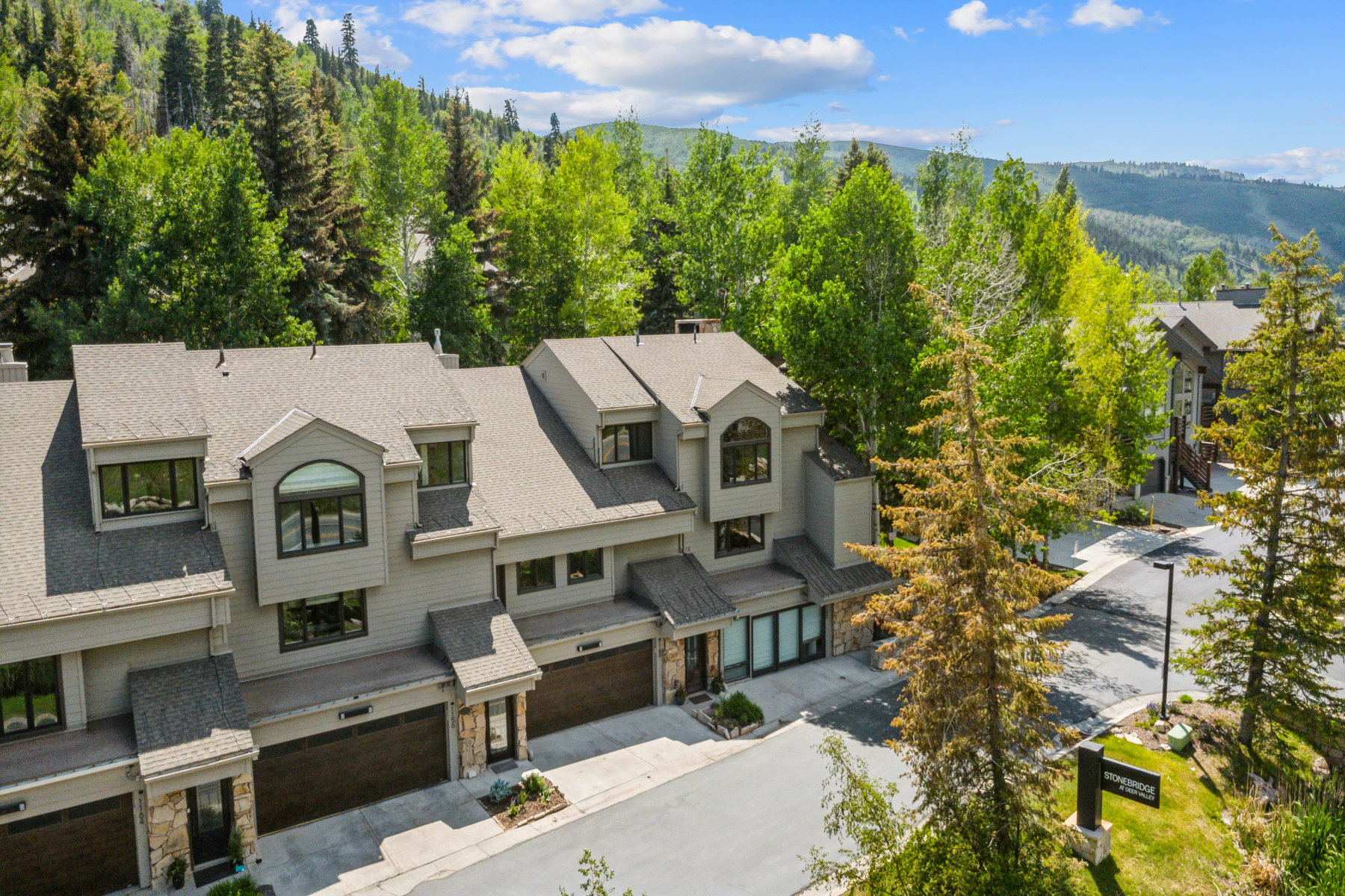 Multi-level townhouse property featuring a neutral-toned exterior, dark garage doors, and stone accents