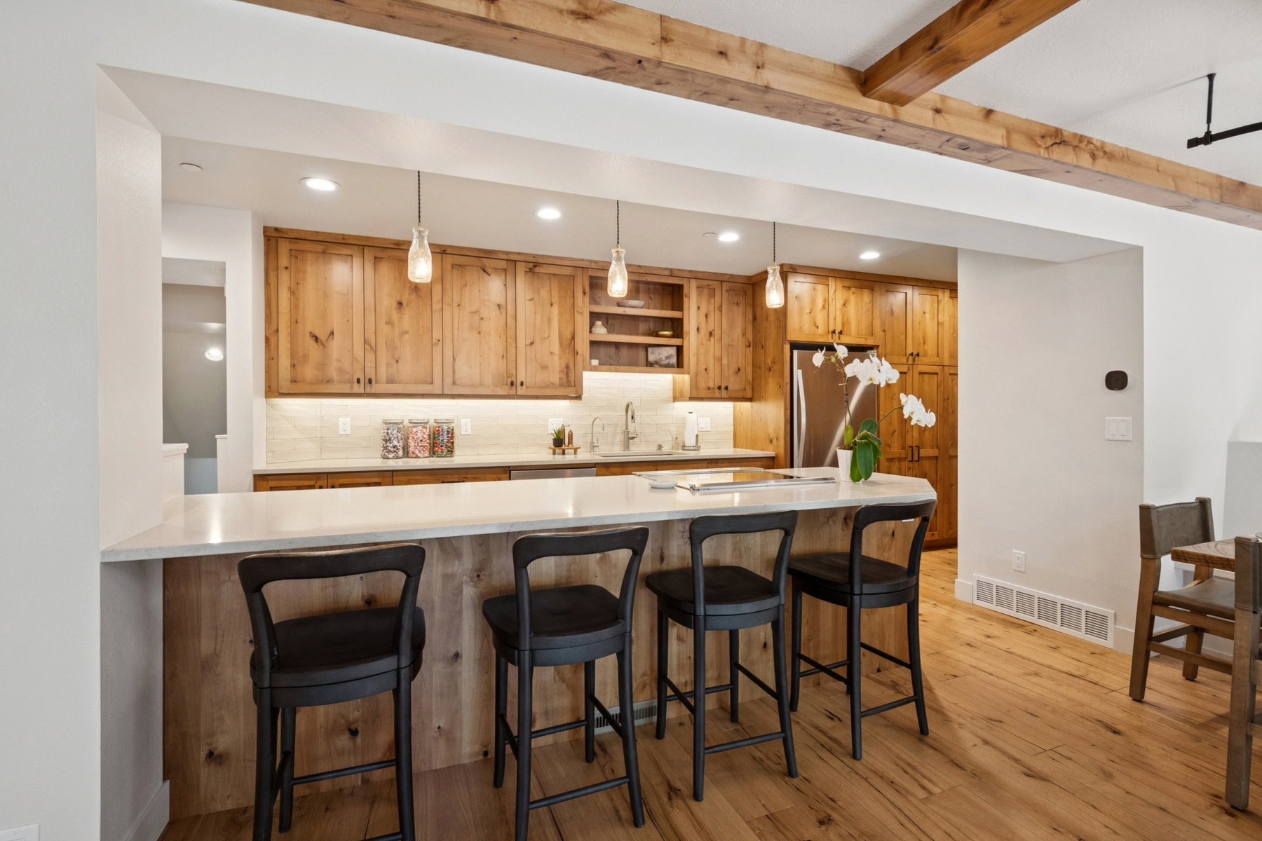 Kitchen featuring a breakfast bar with seating for four, wood-finish cabinetry, stainless steel refrigerator, white countertops, and exposed wood ceiling beams
