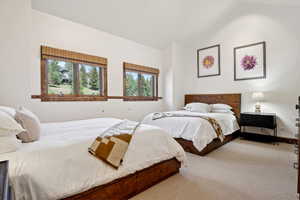 Bedroom featuring a vaulted ceiling and two windows with wood frames and woven shades