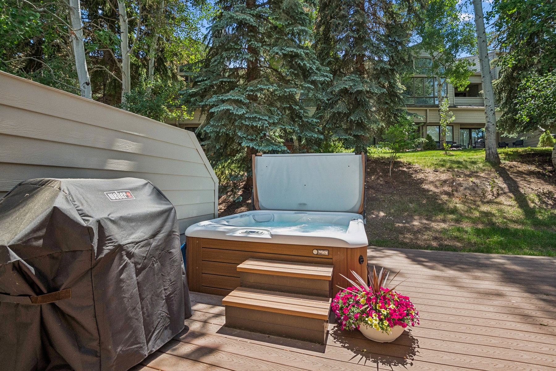 Outdoor deck featuring a hot tub with wood-finish steps and a surrounding natural landscape with mature trees