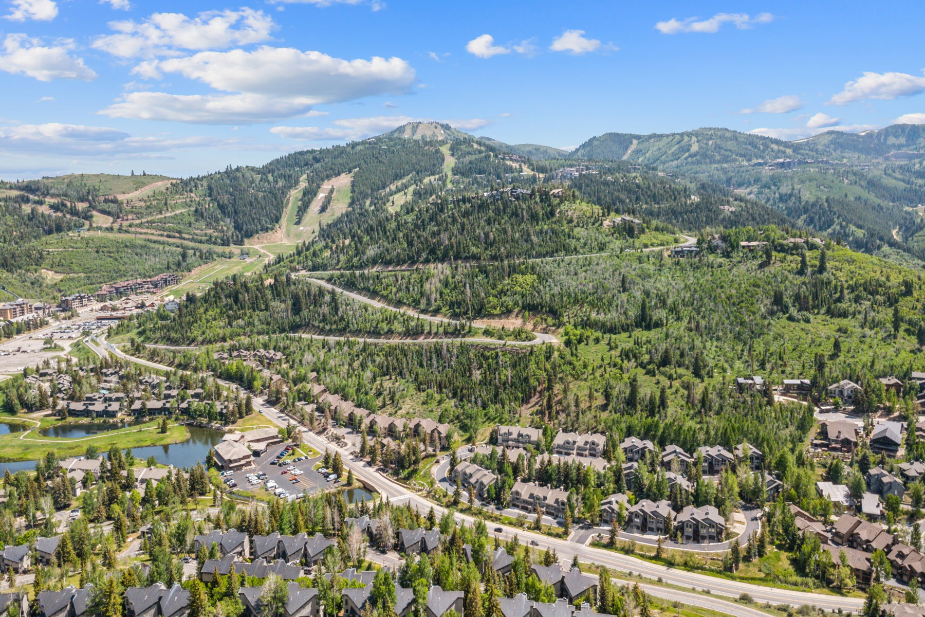 Expansive mountain landscape featuring a ski resort, lush green forests, a private lake, and residential properties with dark roofs
