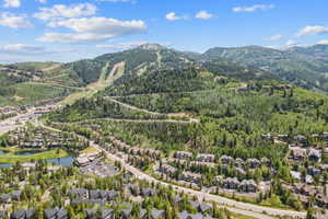 Expansive mountain landscape featuring a ski resort, lush green forests, a private lake, and residential properties with dark roofs