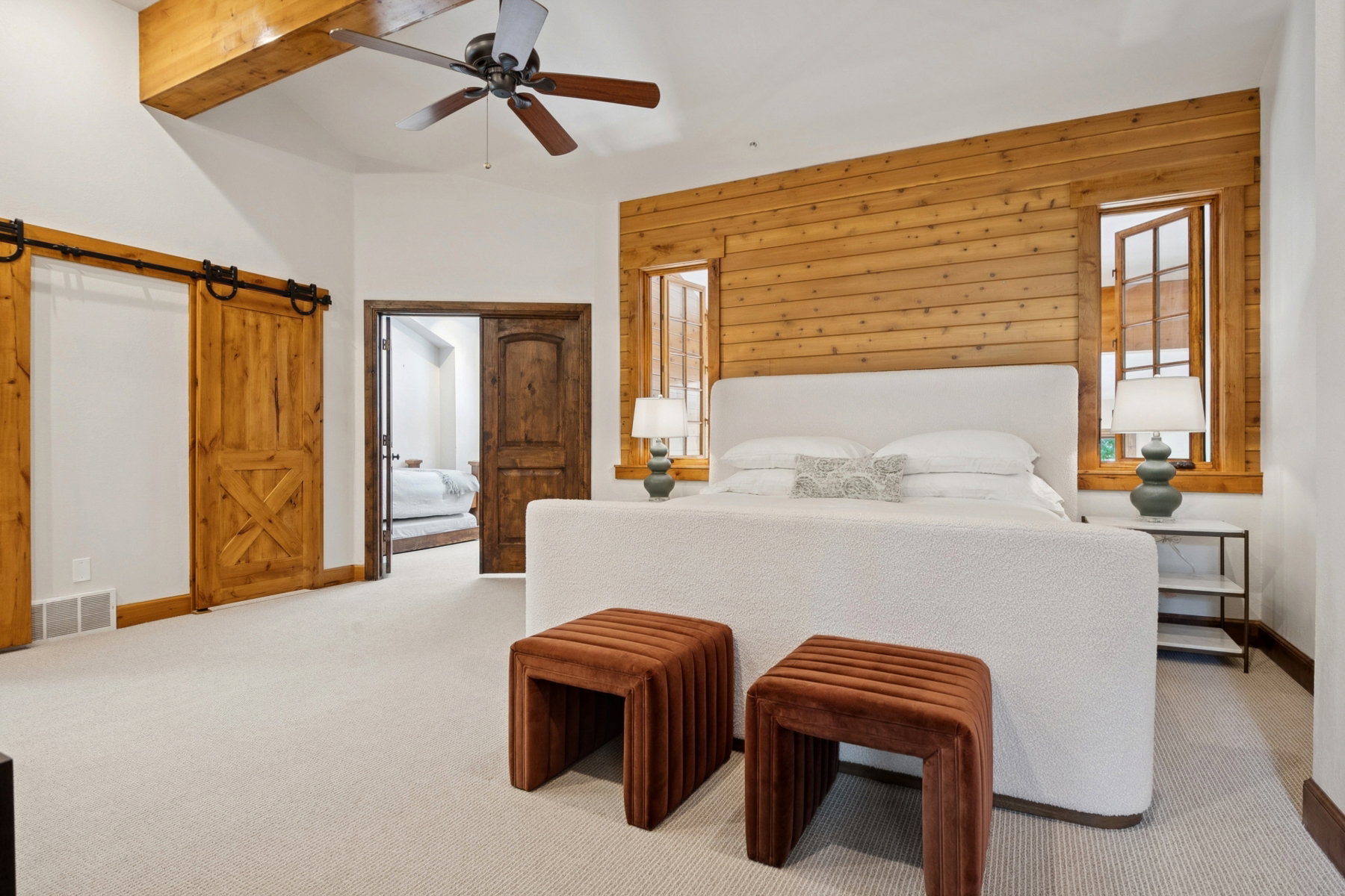Spacious bedroom featuring light neutral carpeting, a wooden accent wall, two framed windows, and a ceiling fan