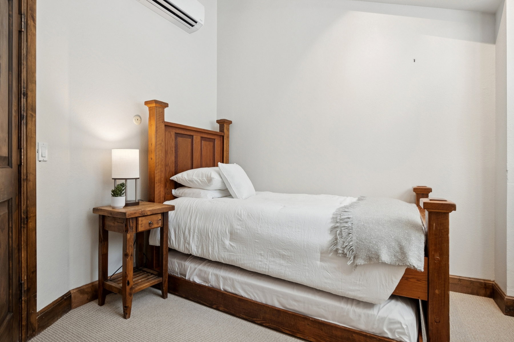 Bedroom featuring a wood-frame bed with a trundle, light carpet, white walls, and a wall-mounted climate control unit