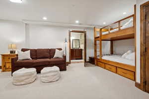 Carpeted room featuring a built-in bunk bed with storage drawers, a recessed lighting, and a wood-paneled doorway leading to a bathroom