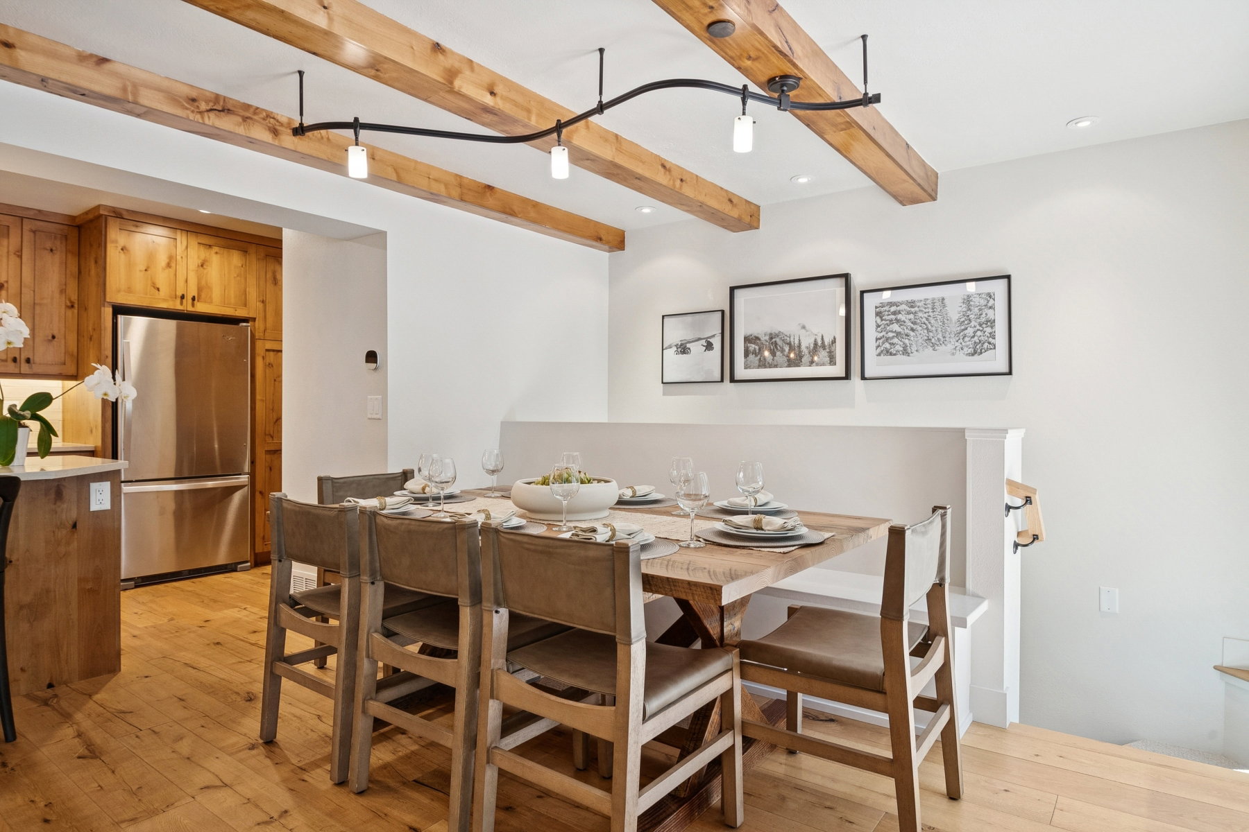 Open-concept dining area featuring wood-finish flooring, exposed ceiling beams, and a built-in banquette