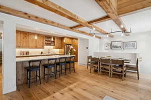 Open-concept kitchen and dining area featuring wood-finish flooring, exposed ceiling beams, and recessed lighting