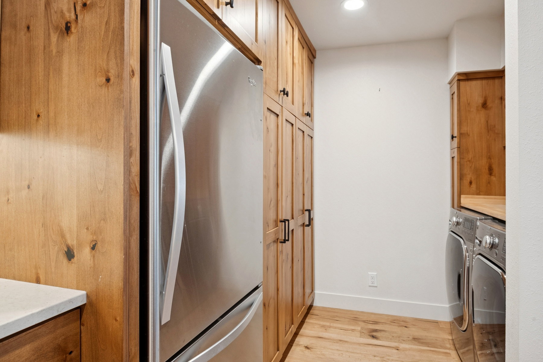 Full-height wood cabinetry with matte black hardware, stainless steel refrigerator, wood-finish flooring, recessed lighting, and white walls