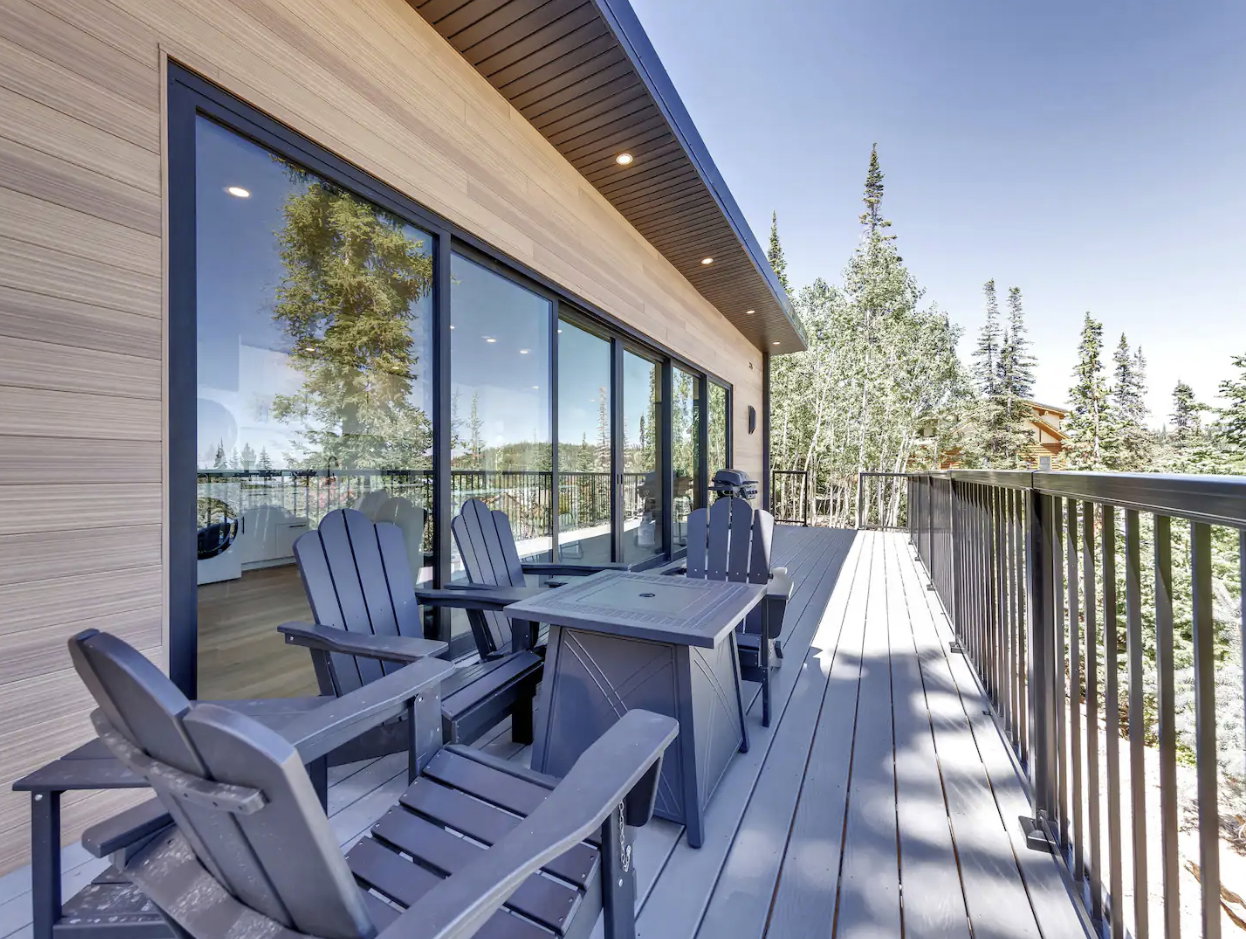 Spacious outdoor deck featuring light-toned composite decking, black metal railings, and natural wood-tone horizontal siding