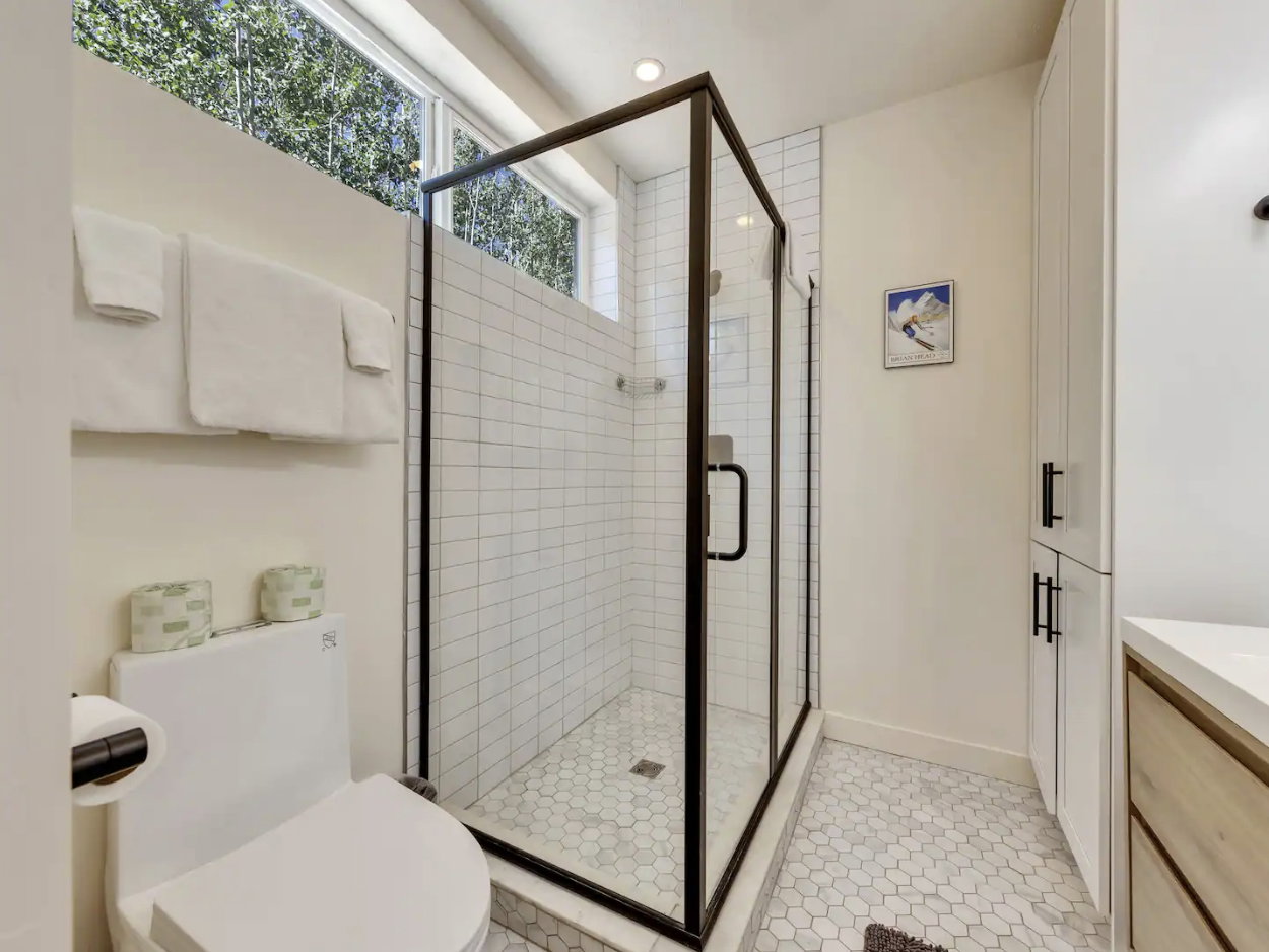 Modern bathroom featuring a glass-enclosed shower with black framing, white subway tile shower walls, and white hexagonal floor tiling