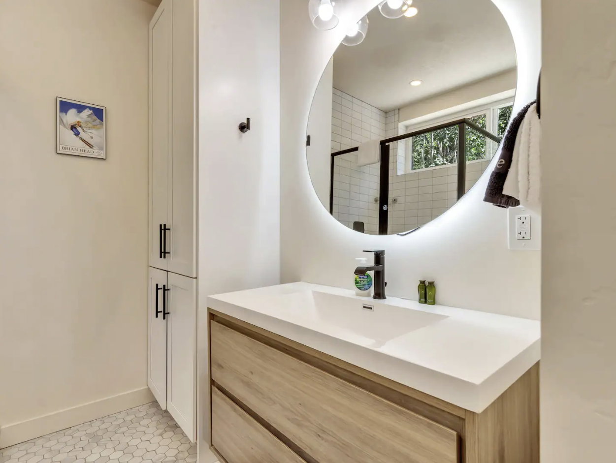 Modern bathroom featuring a wood-finish vanity with an integrated white sink and a back-lit round mirror