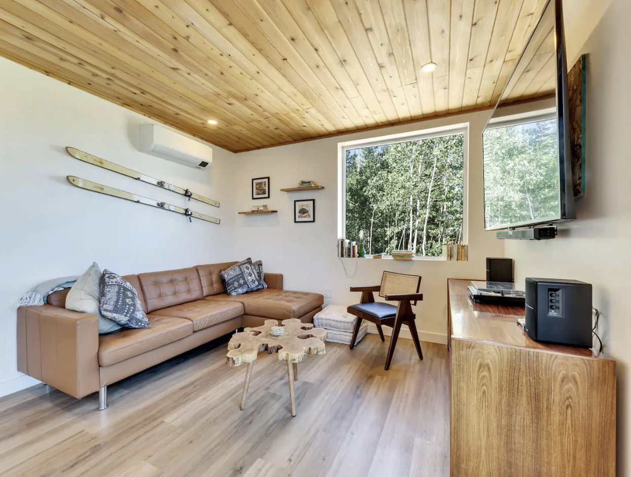 Inviting living area featuring a plank wood ceiling, light wood-finish flooring, and a large window overlooking trees