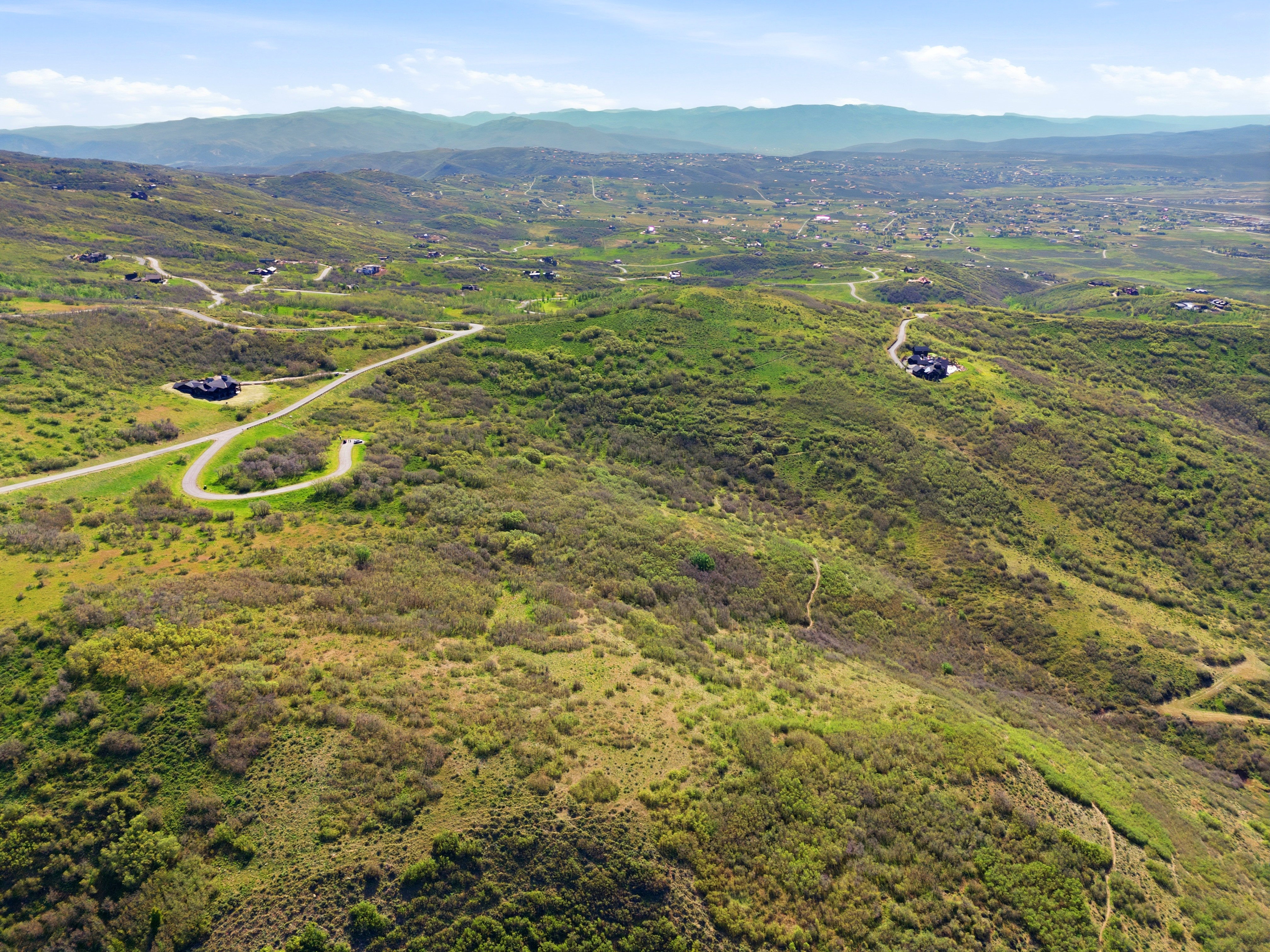 Expansive hillside property featuring scattered residences and winding roadways amidst natural green landscaping