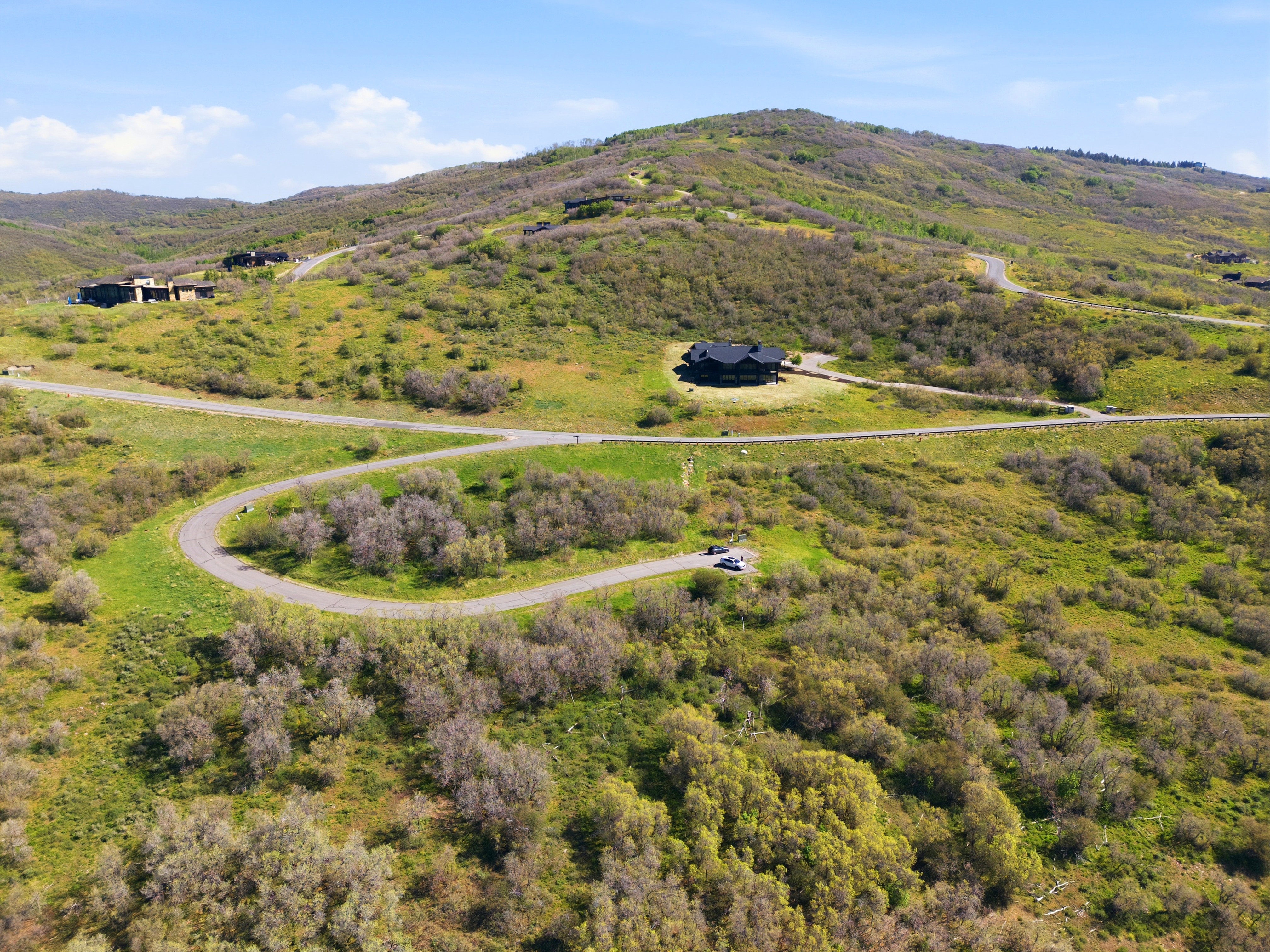 Expansive hillside property featuring a paved road, scattered natural vegetation, and distant residential structures
