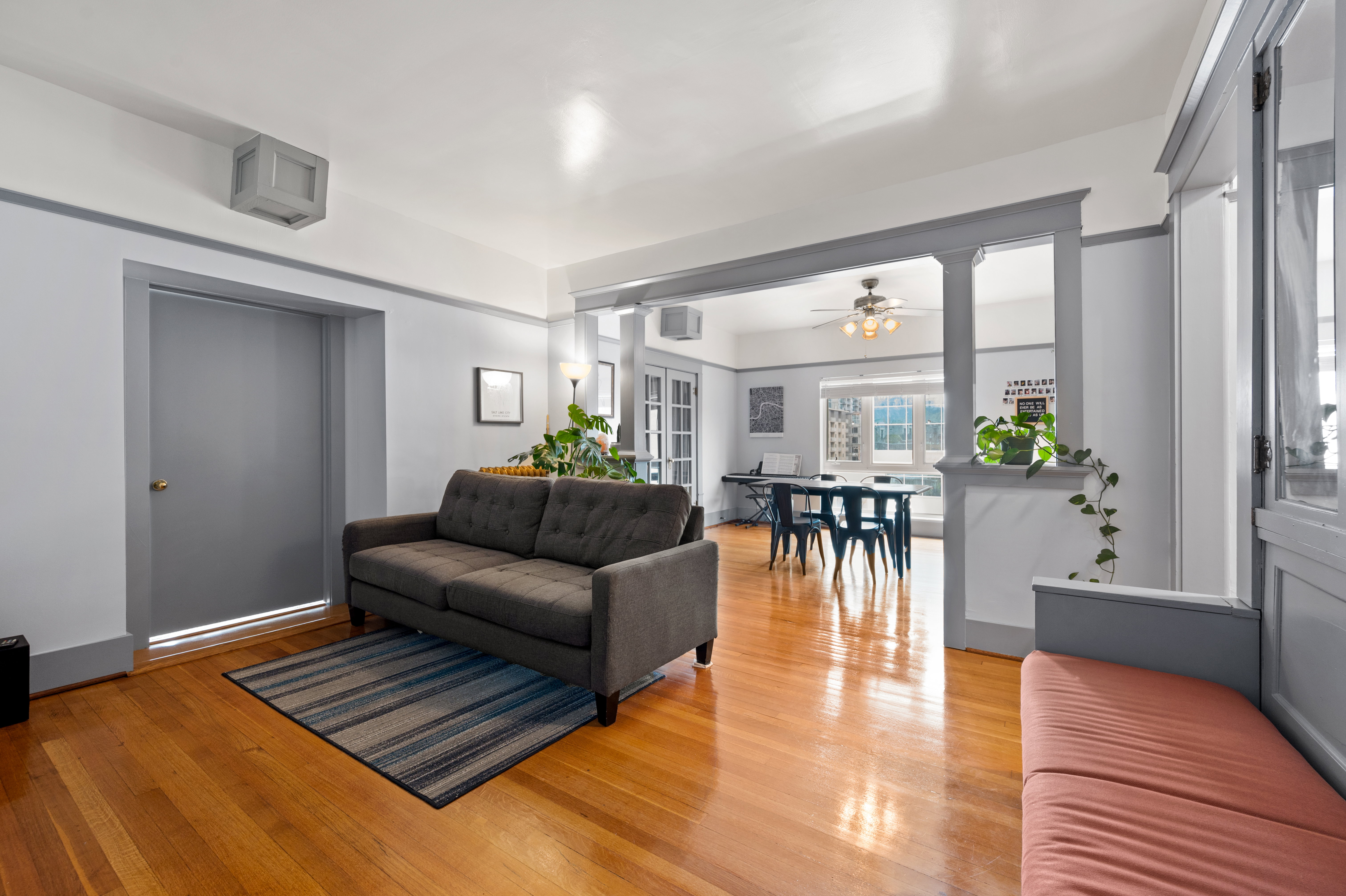 Spacious living area featuring polished wood-finish flooring, a neutral color palette with contrasting trim, and an archway with decorative columns leading to an additional space
