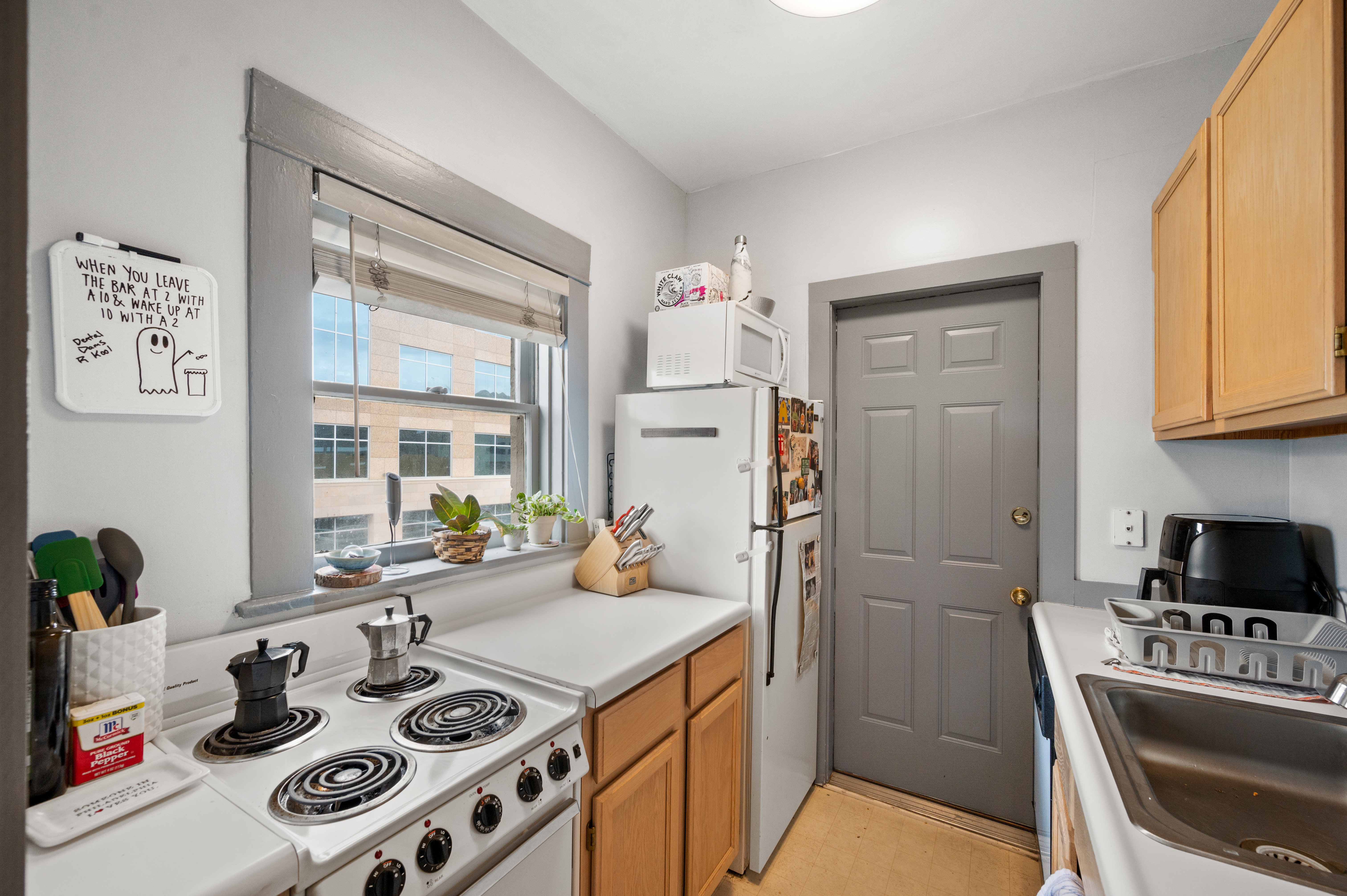 Compact kitchen featuring a white electric range, wood-finish cabinetry, a stainless steel sink, and a multi-pane window