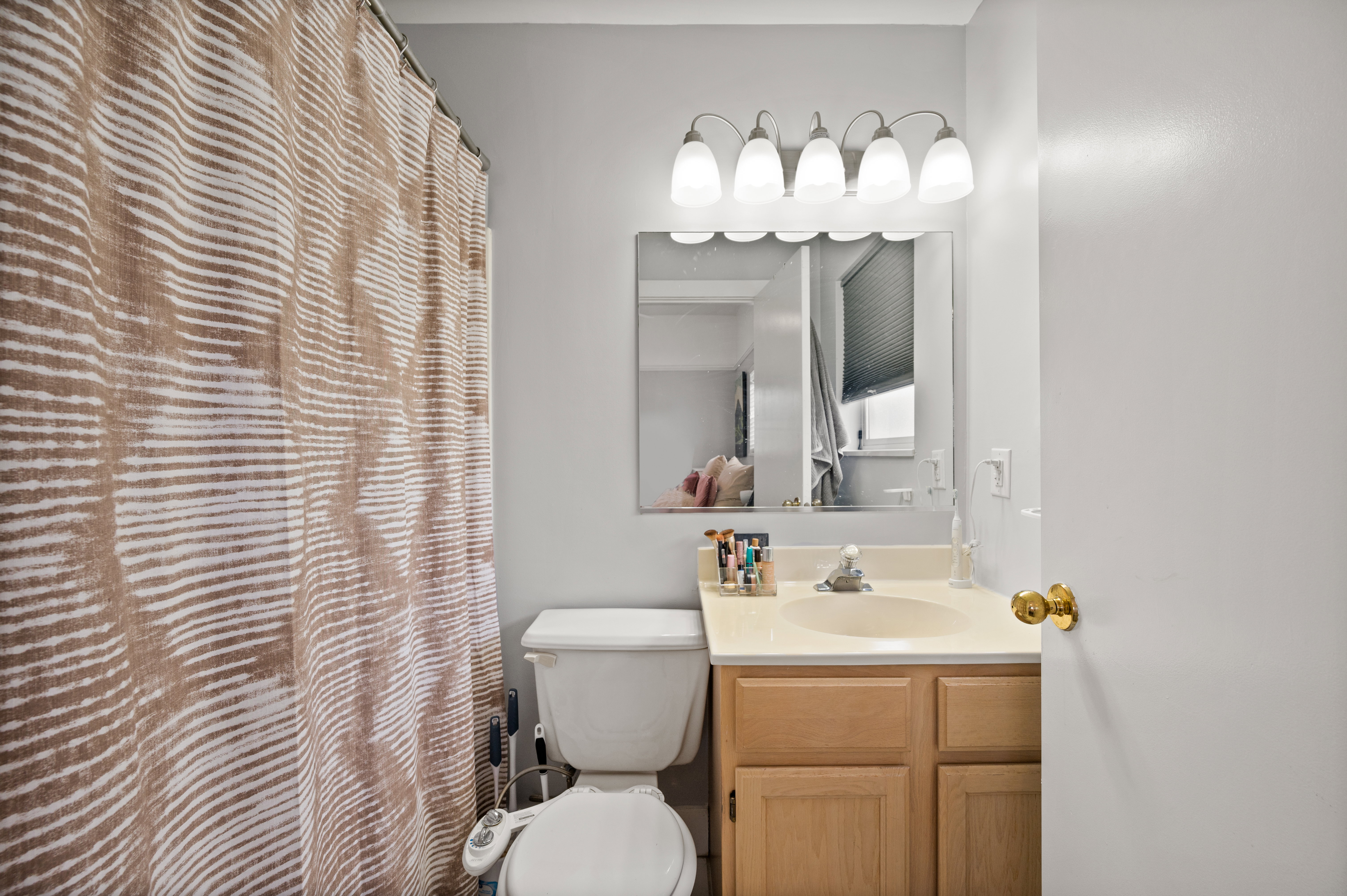 Full bathroom featuring a single vanity with wood-finish cabinetry and a light-toned countertop, a wall-mounted mirror, and a five-light fixture