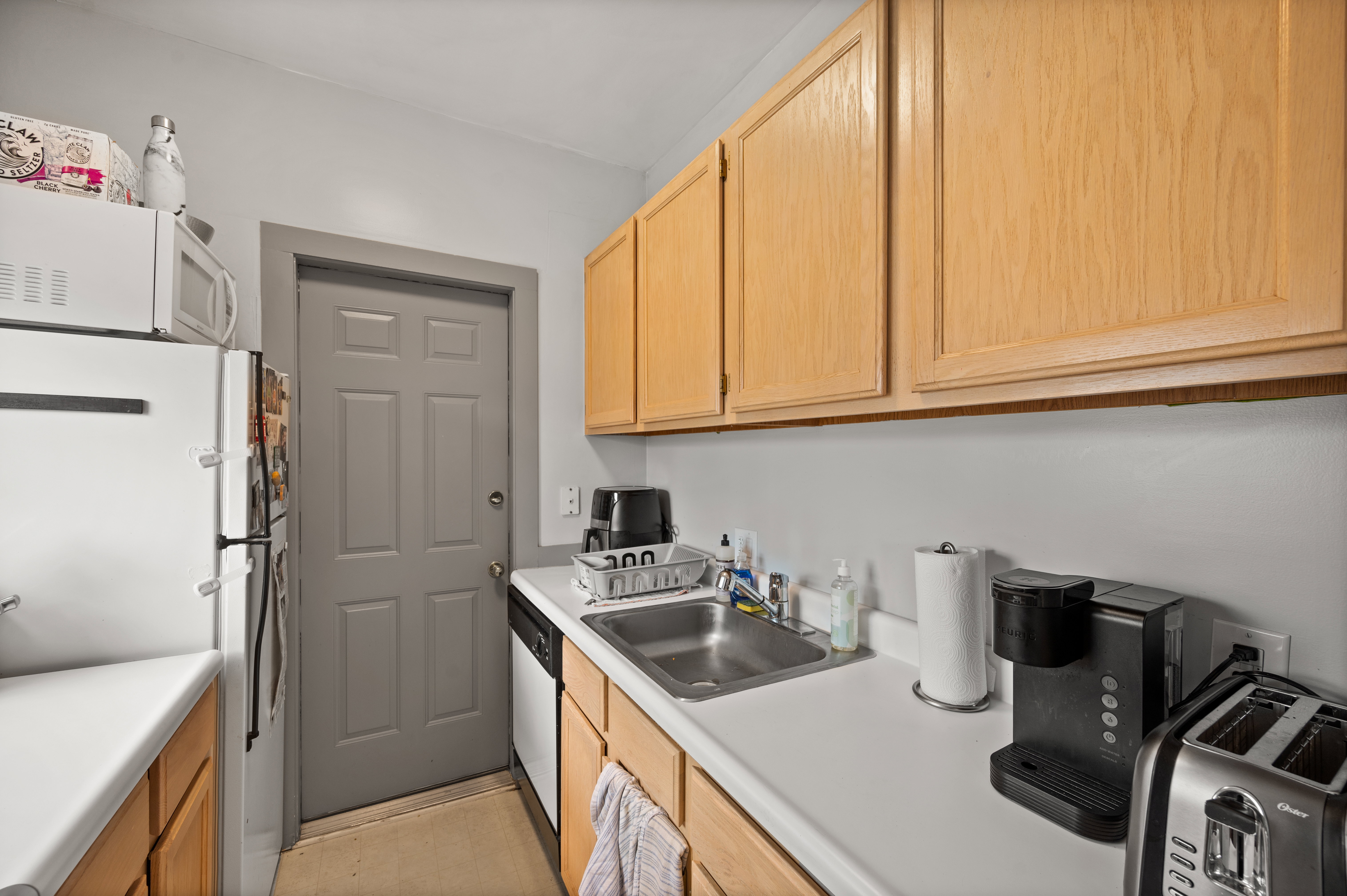 Kitchen featuring light wood-finish cabinetry, white countertops, stainless steel sink, and a four-panel interior door
