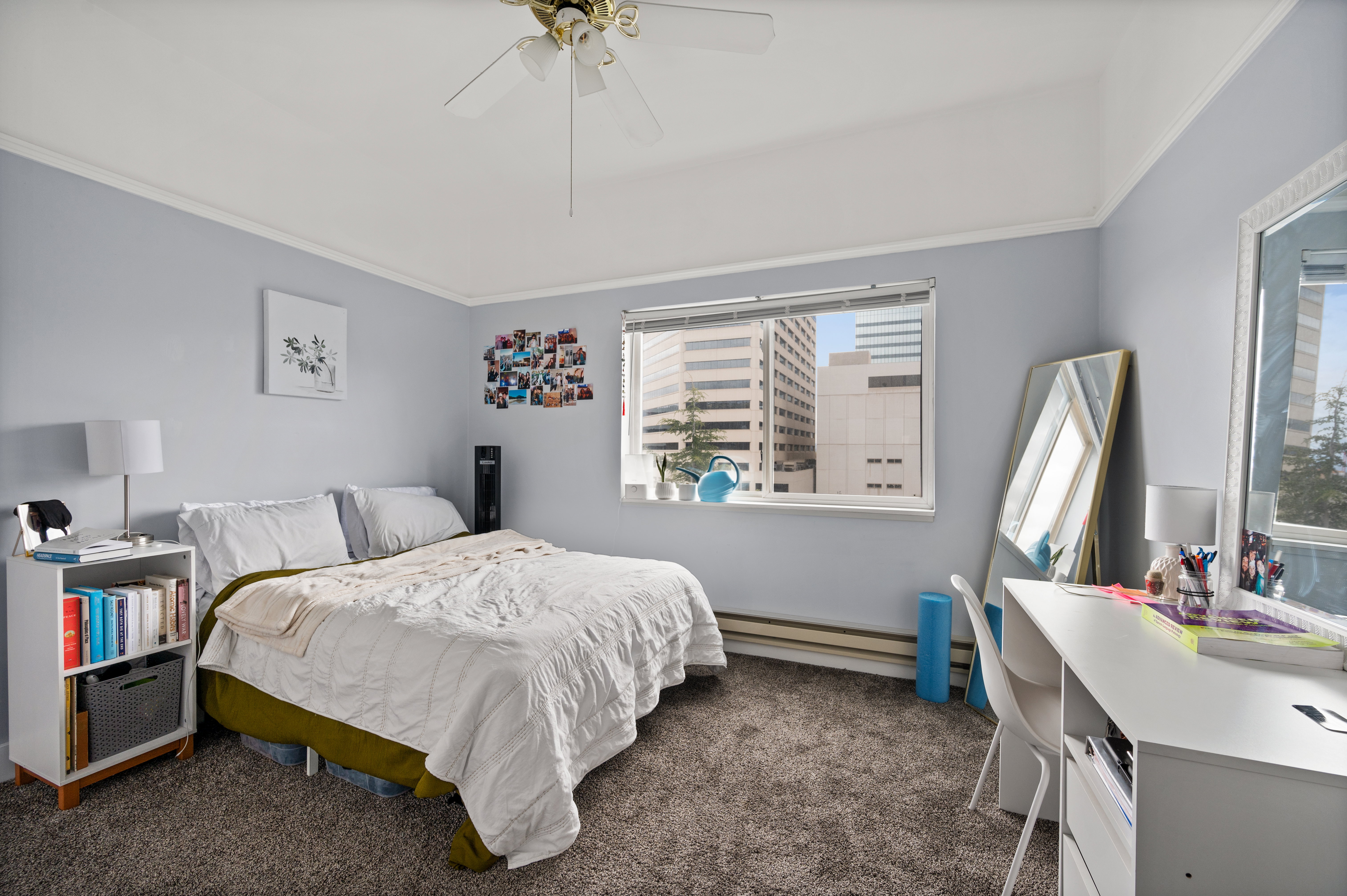 Bedroom featuring neutral wall colors, textured carpeting, a white ceiling fan, and a window offering cityscape views